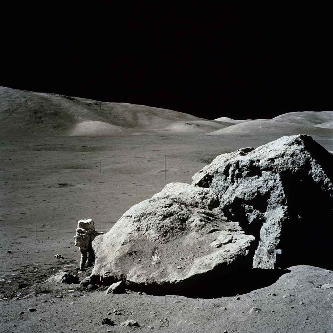 航天图片资料 · An astronaut in a space suit stands on the lunar surface next to a large lunar boulder.