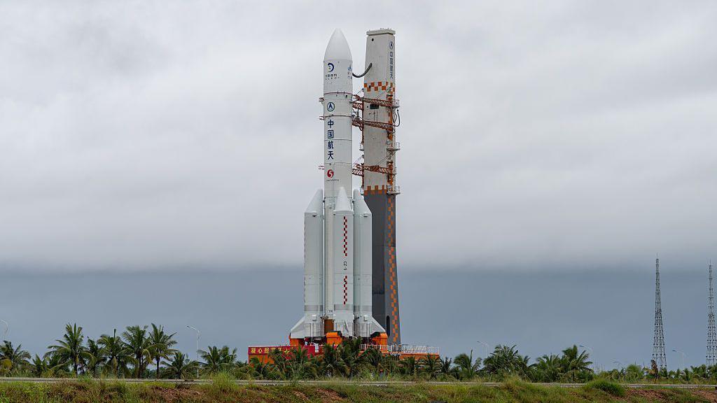 航天图片资料 · A white spacecraft standing. There are trees and grass around the bottom of it.