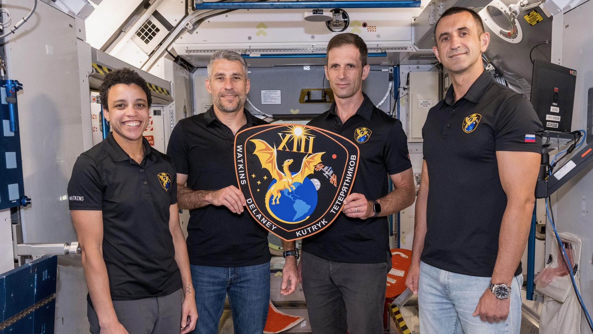 航天图片资料 · three men and one woman, all wearing black polo shirts, hold a plaque inside a mockup space module