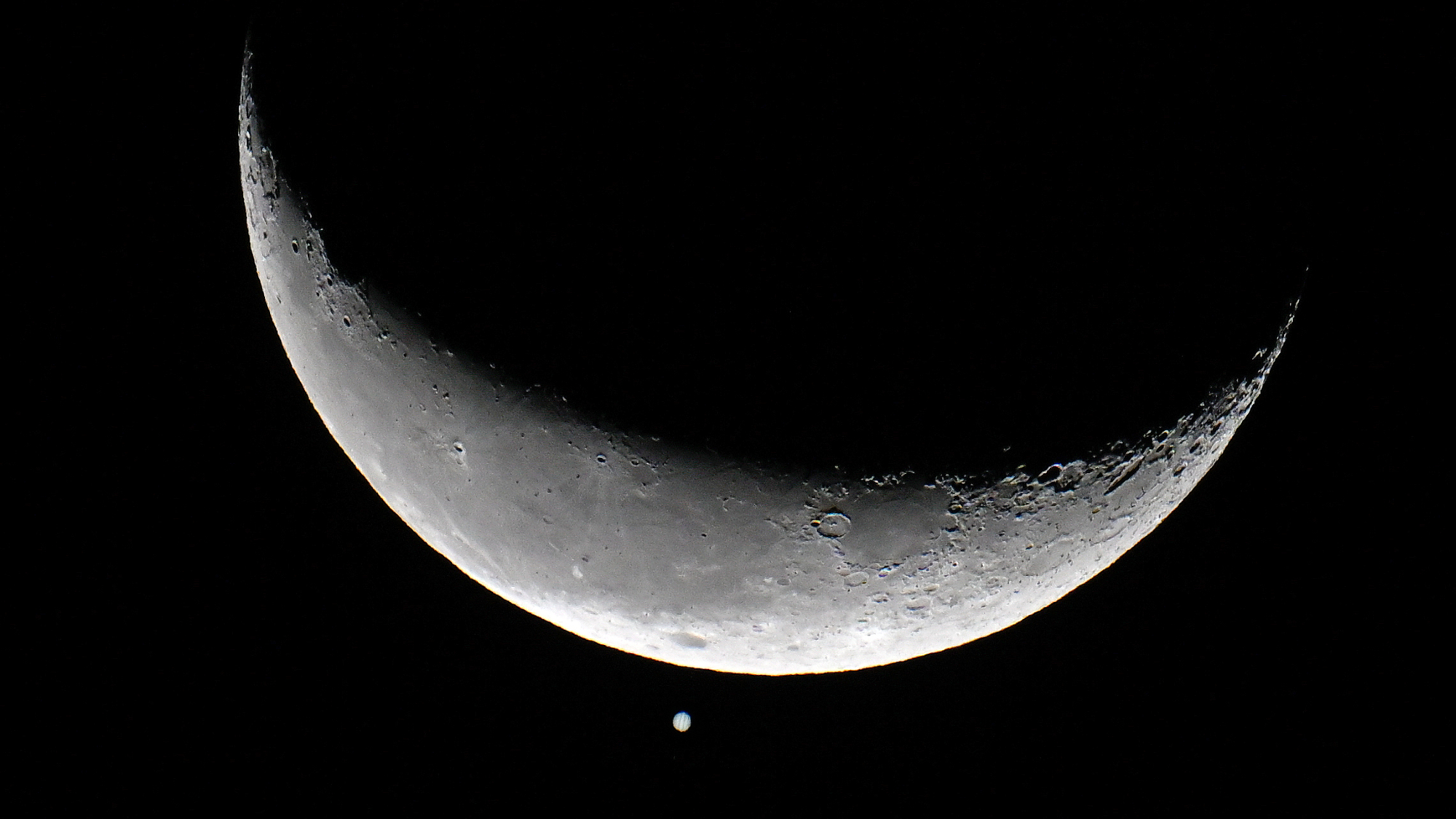 航天图片资料 · The crescent moon is shown in a black night sky with a bright point of light representing Jupiter positioned below its sunlit crescent.