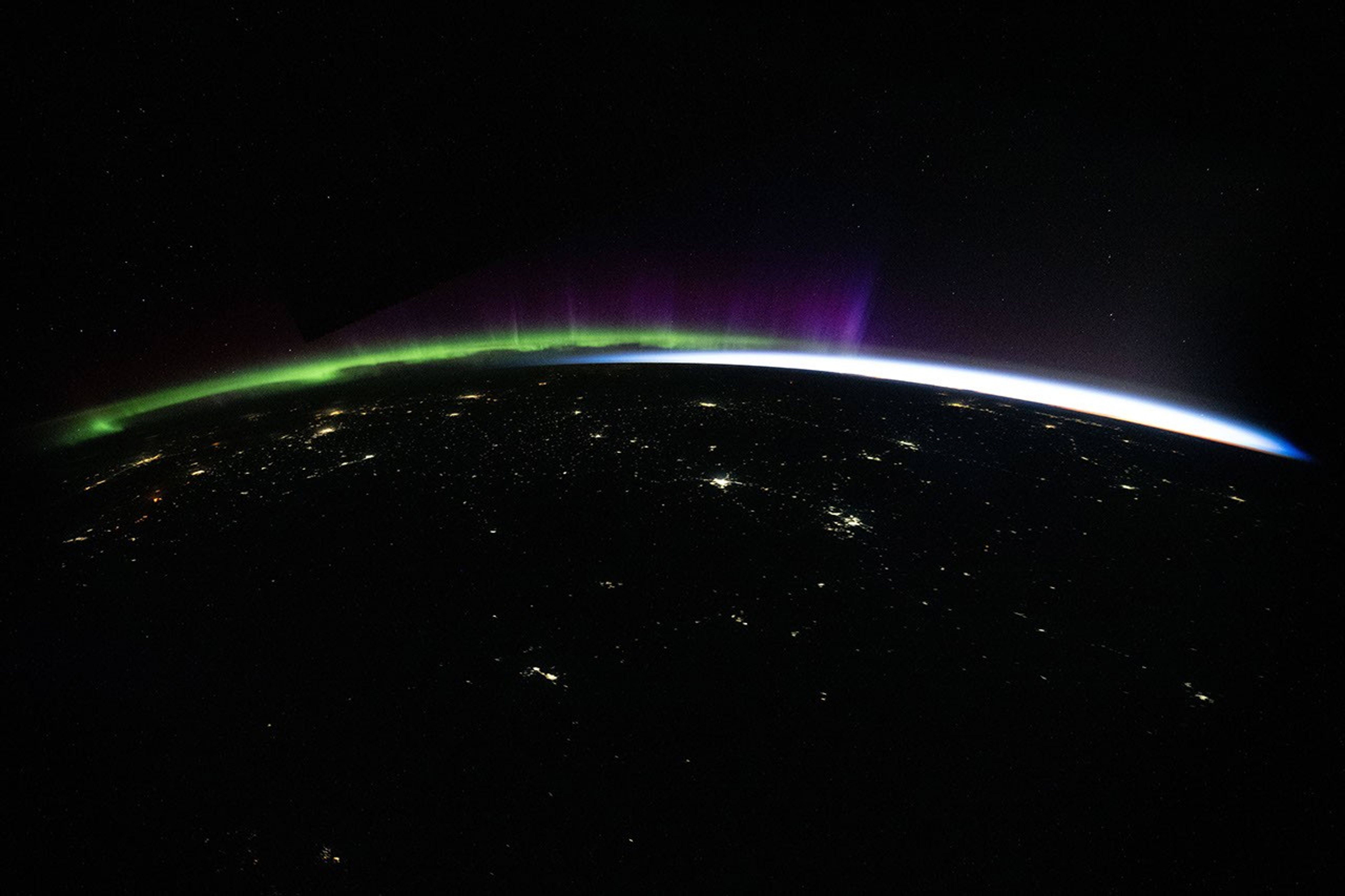 航天图片资料 · Green and purple aurora and white airglow arc above Earth’s limb and the scattered city lights of Central Asia in a nighttime photo taken from the International Space Station.