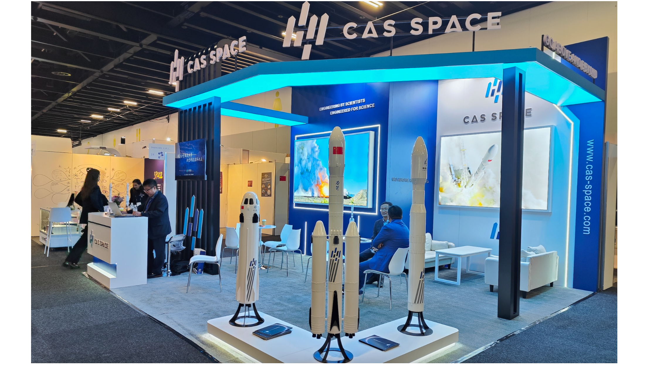 航天图片资料 · a booth in an exhibition hall at a space conference, showing three white model rockets on a white platform with a few people in the background