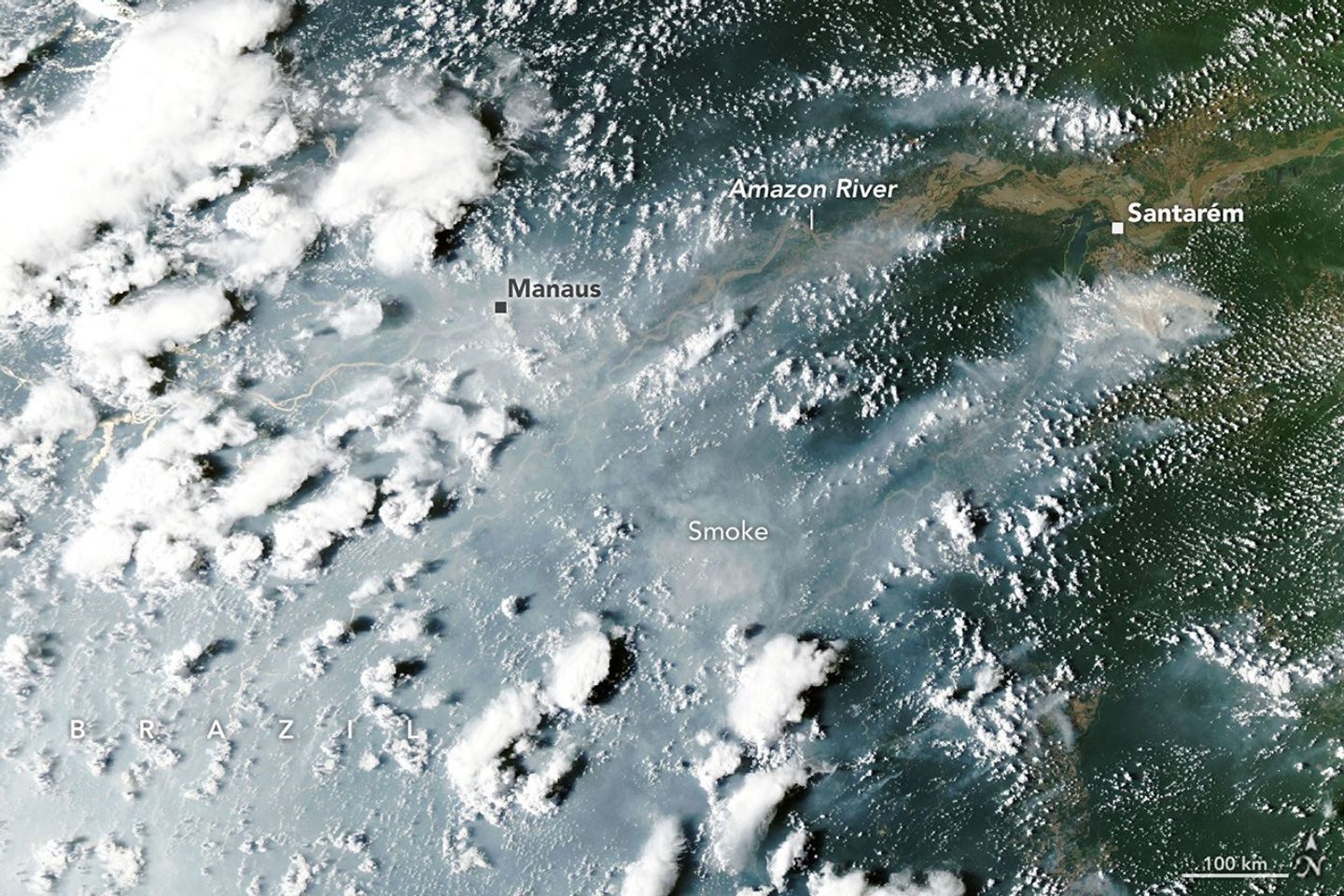 航天图片资料 · Thick gray smoke partially obscures the Amazon River and surrounding rainforest near the cities of Manaus and Santarém. Puffy white clouds rise above the smoke on the left side of the image.