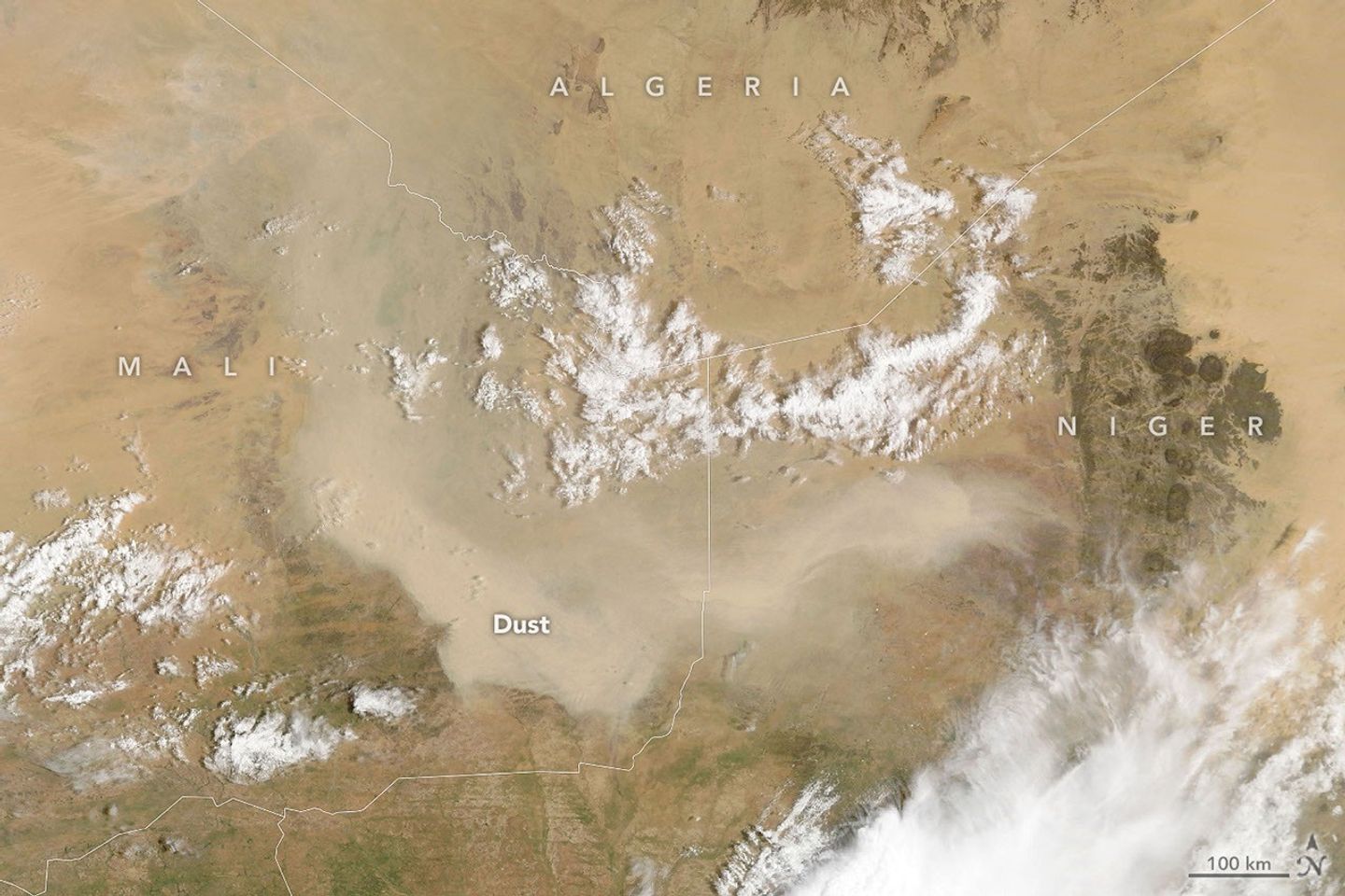 航天图片资料 · A light brown dust plume, dense at its center and more diffuse toward its edges, extends horizontally across an orange-brown and green landscape. Scattered white clouds cover some of the scene.