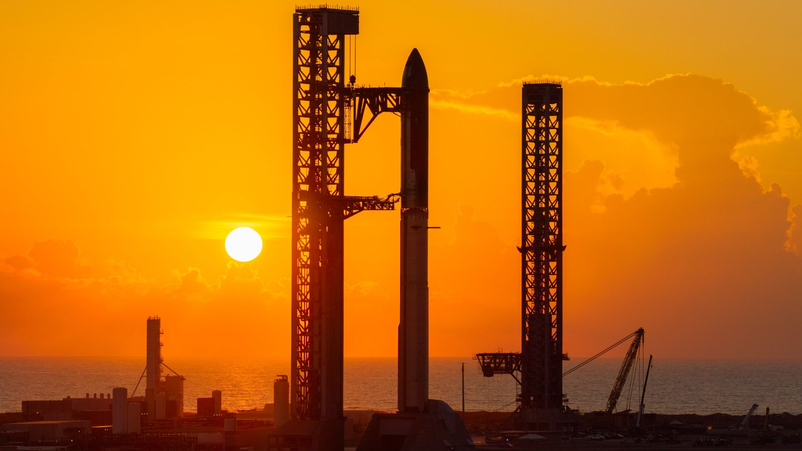 航天图片资料 · A towering SpaceX Starship rocket stands at Starbase's Pad 2, silhouetted against a yellow sky and rising sun.