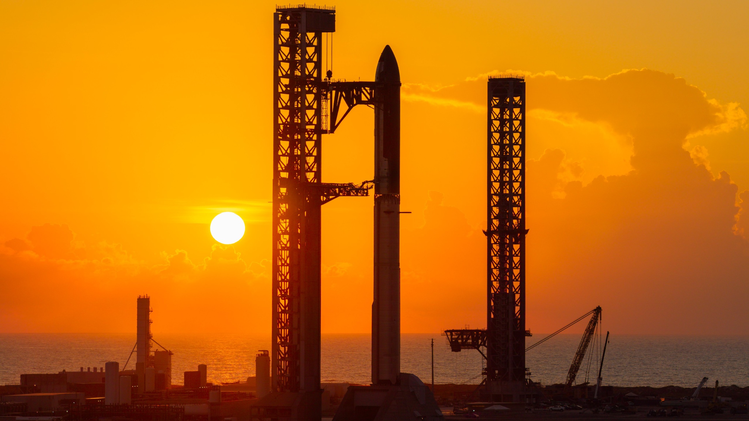 航天图片资料 · A towering SpaceX Starship rocket stands at Starbase's Pad 2, silhouetted against a yellow sky and rising sun.
