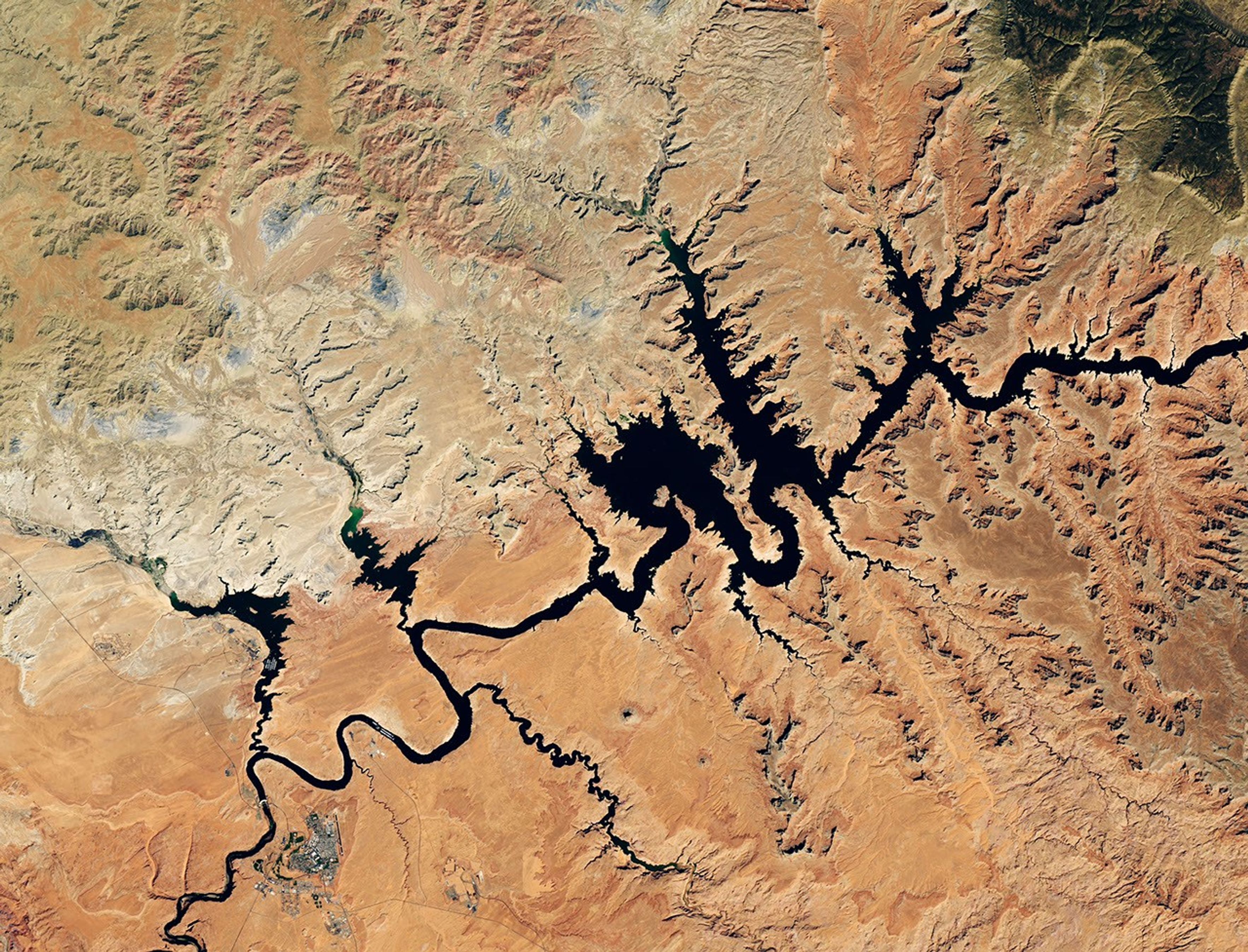 航天图片资料 · Water in Lake Powell is at record-low levels and looks like a wide river winding through a light orange desert landscape. The Glen Canyon Dam and the town of Page, Arizona, are visible in the lower left.