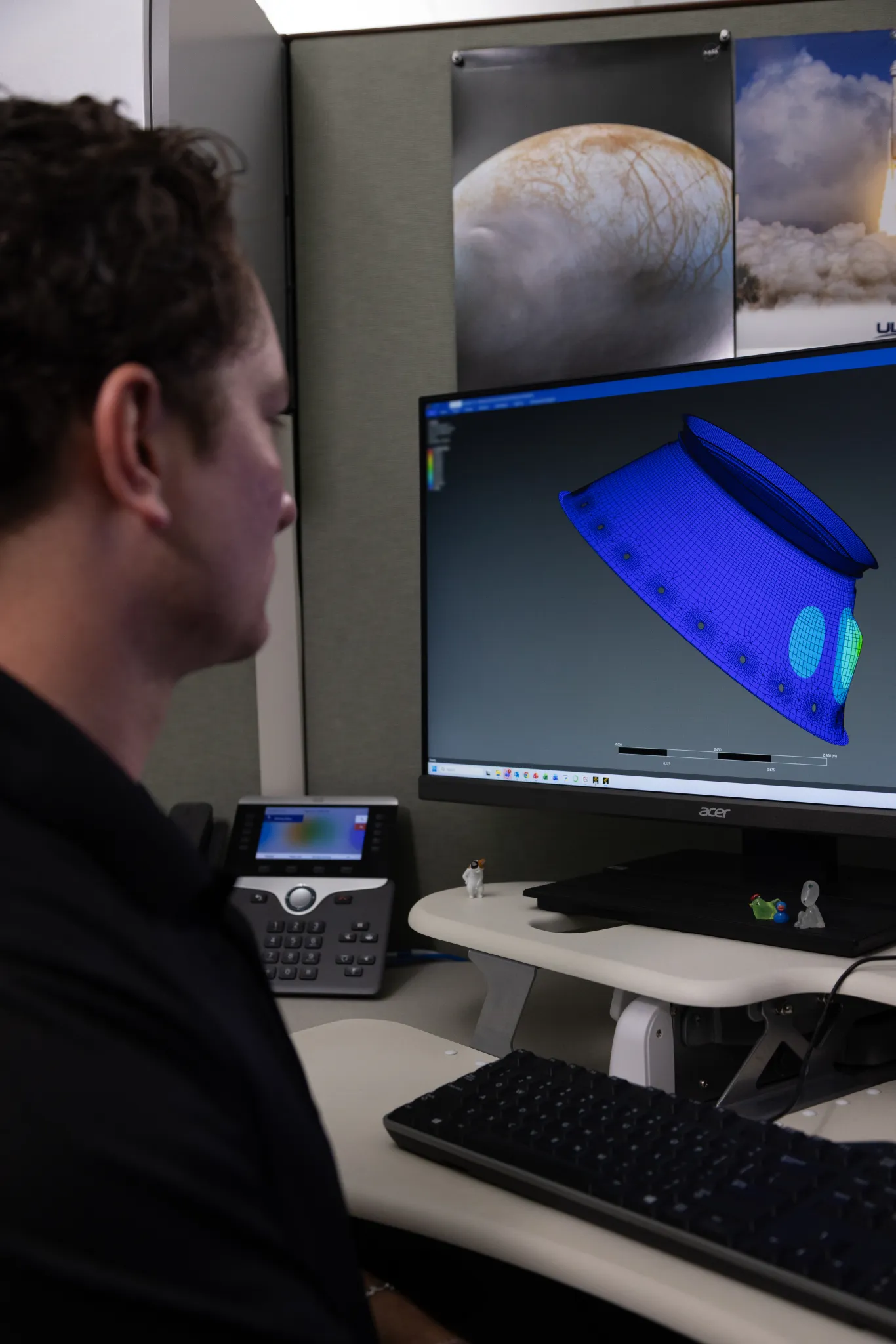 航天图片资料 · A person sits at a workstation viewing a computer monitor that displays a blue 3D wireframe engineering model of a spacecraft component.