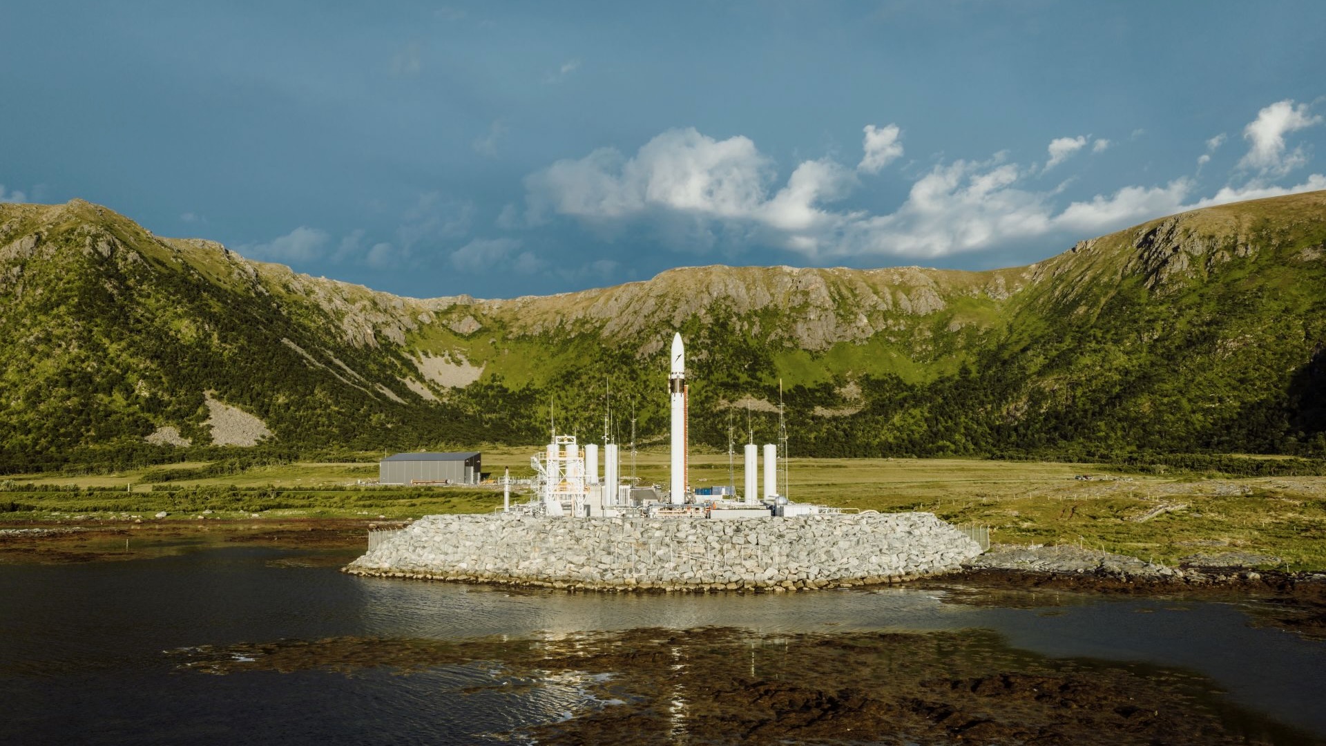 航天图片资料 · a white rocket stands on a seaside pad with green mountains in the background