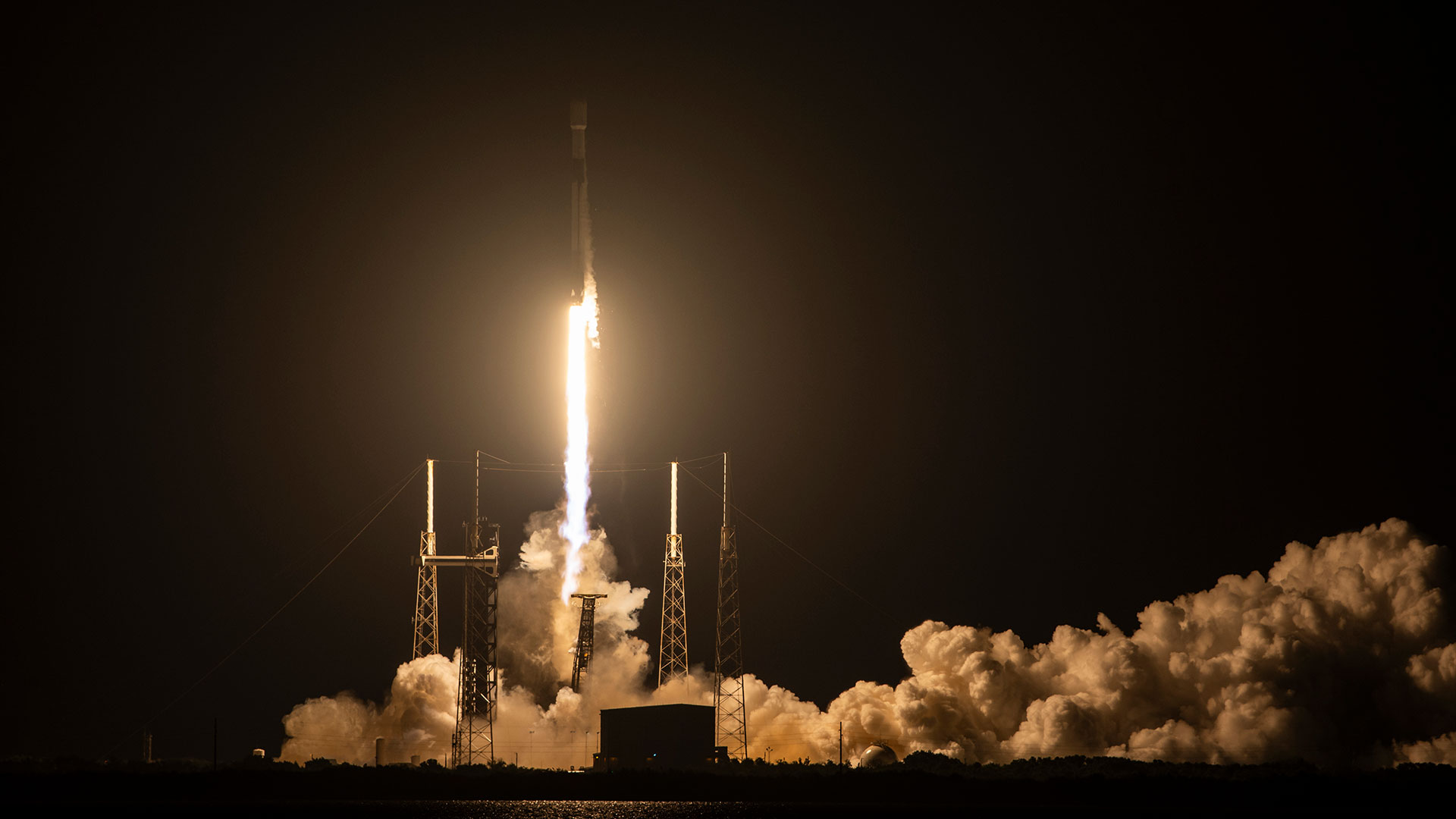 航天图片资料 · The bright orange-white plume from a rocket lights up its launch pad as it lifts off into the darkness of an early morning sky.