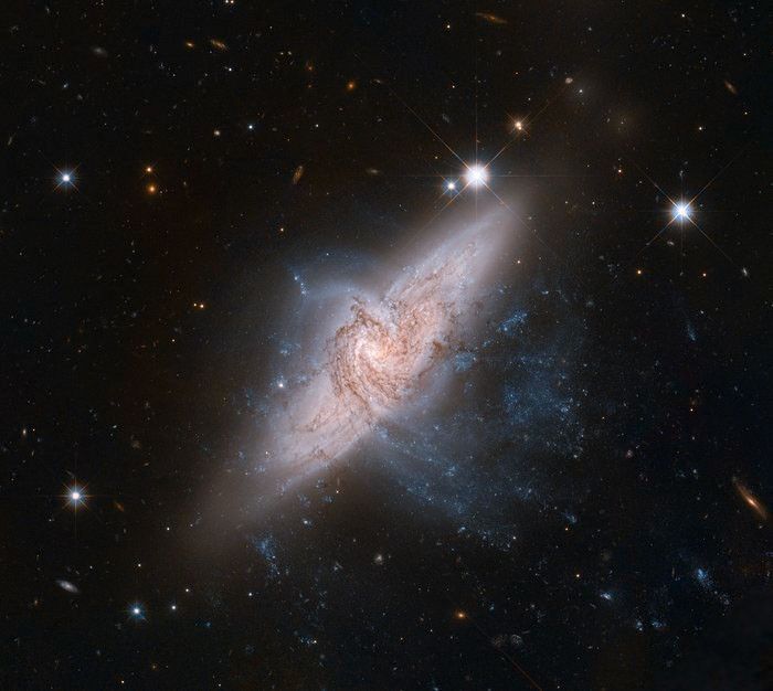 航天图片资料 · A space telescope view showing two large spiral galaxies, lined up one in front of the other. The foreground pinwheel-shaped galaxy is seen nearly face-on, with dark, swirling lanes of interstellar dust silhouetted against the bright glow of a larger background galaxy. The background galaxy is tilted both away from the viewer and roughly 45 degrees down to the left.