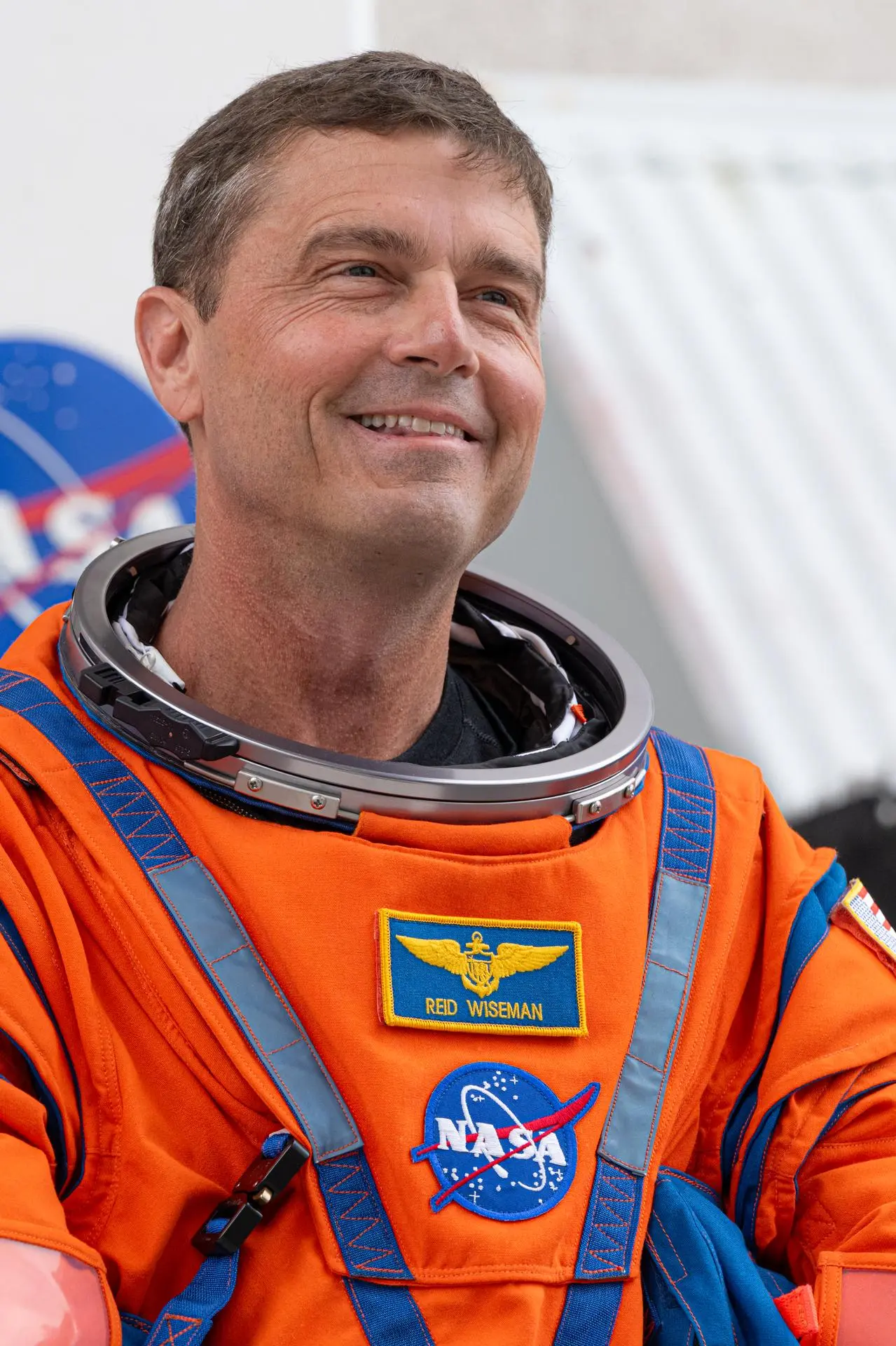 航天图片资料 · Reid Wiseman looks toward supporters, smiling, wearing an orange spacesuit with his name and a NASA meatball patch.