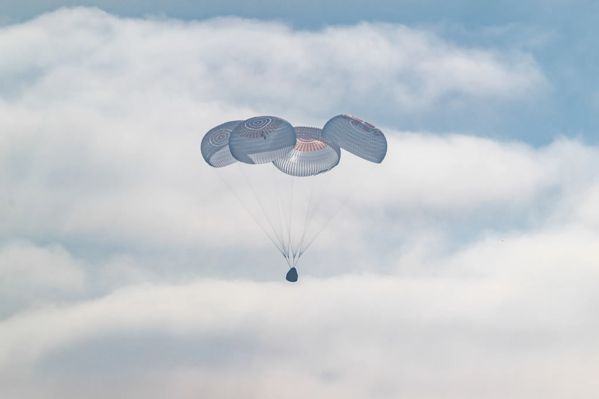 航天图片资料 · A cone-shaped spacecraft and the four large parachutes attached to it against a backdrop of fluffy white clouds in the sky.