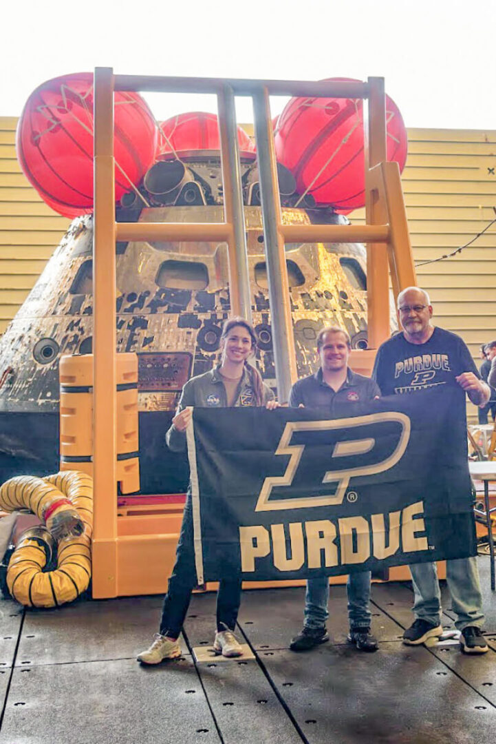 航天图片资料 · Purdue alums Emily Spreen, Jason Endsley and Rob Lantz hold up a Purdue flag in front of the Orion capsule after it returned from its journey to the moon