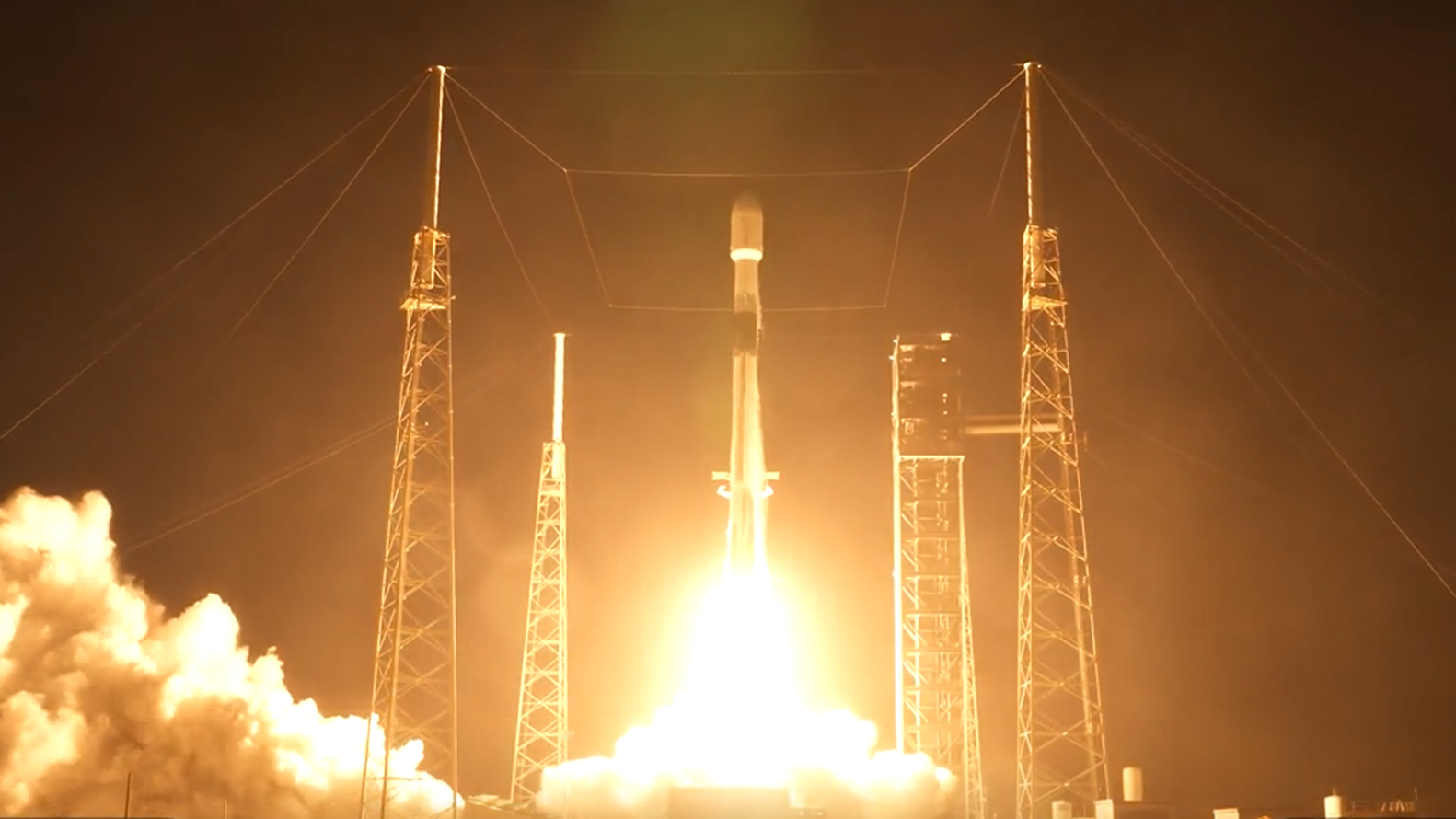 航天图片资料 · A white rocket blasts off a launch site in the dark early morning.