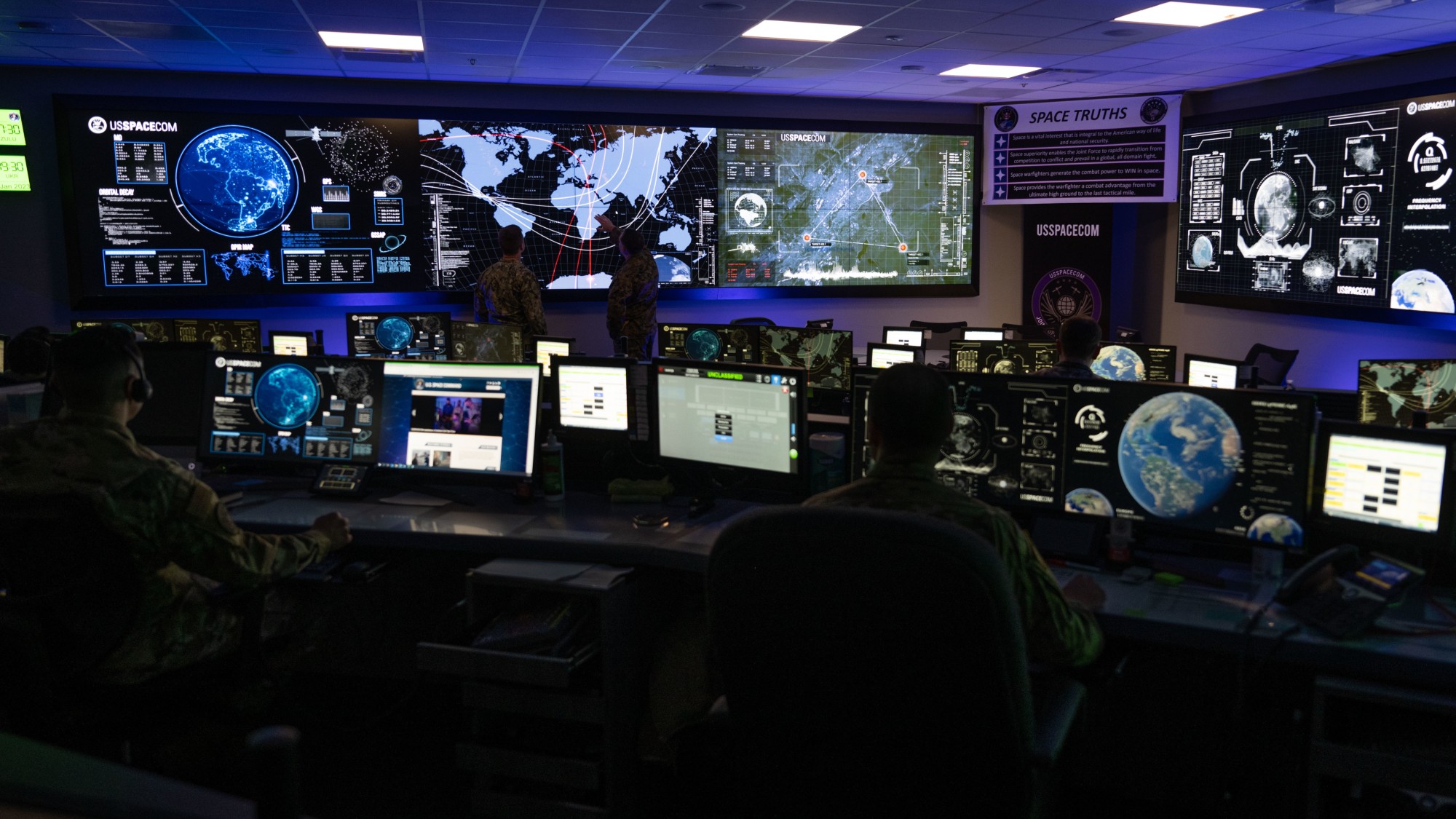 航天图片资料 · people in military fatigues sit behind computer consoles in a room full of screens showing earth and charts of satellites in orbit