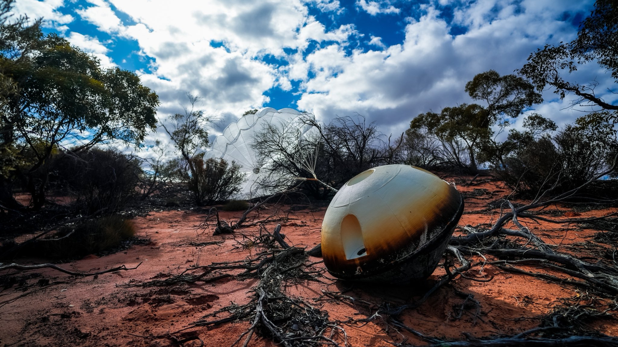 航天图片资料 · a charred space capsule sits on the desert ground surrounded by brush