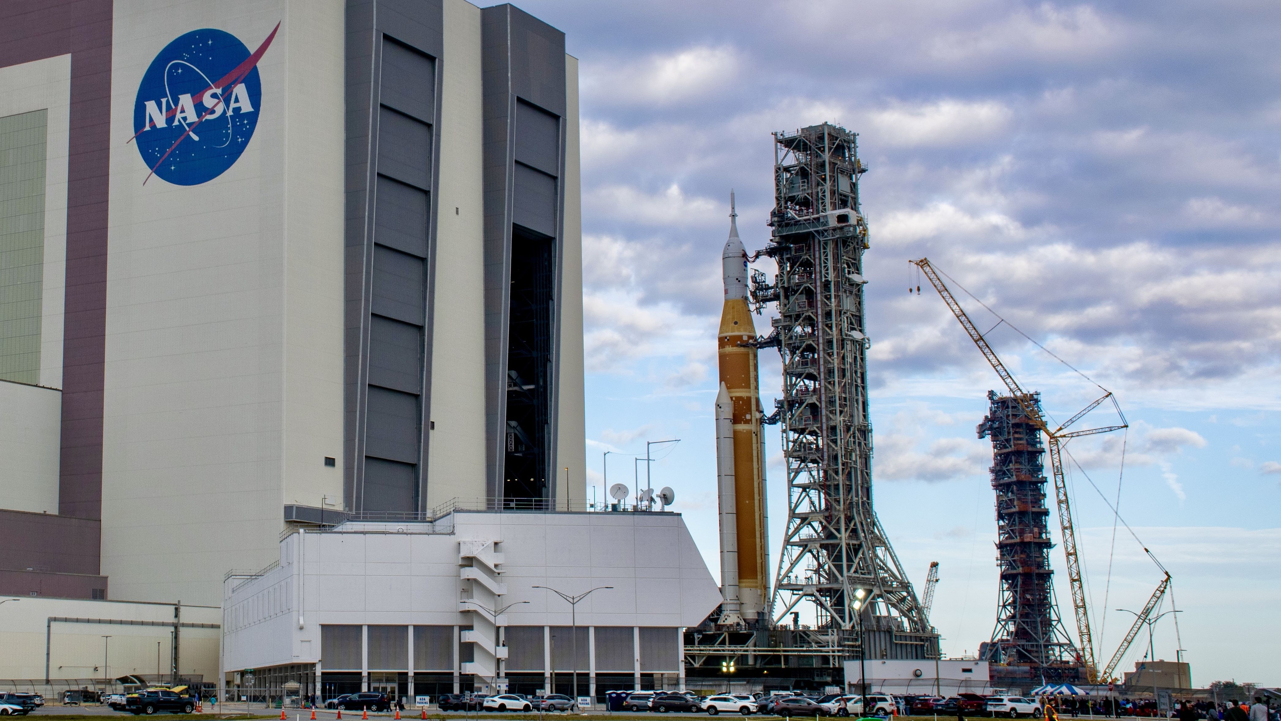 航天图片资料 · A bit orange rocket rolls out of a giant white building, with an extra launch tower in the background.