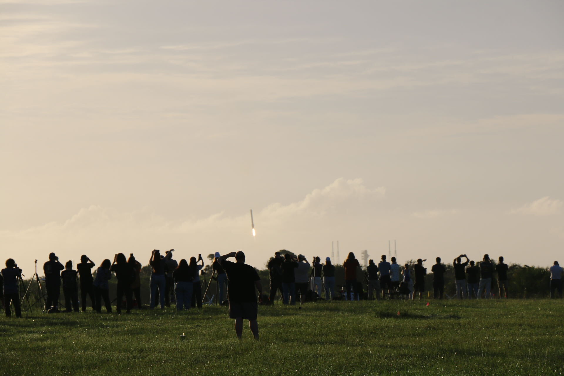 航天图片资料 · People stand on a lawn watching a long structure descend to Earth.