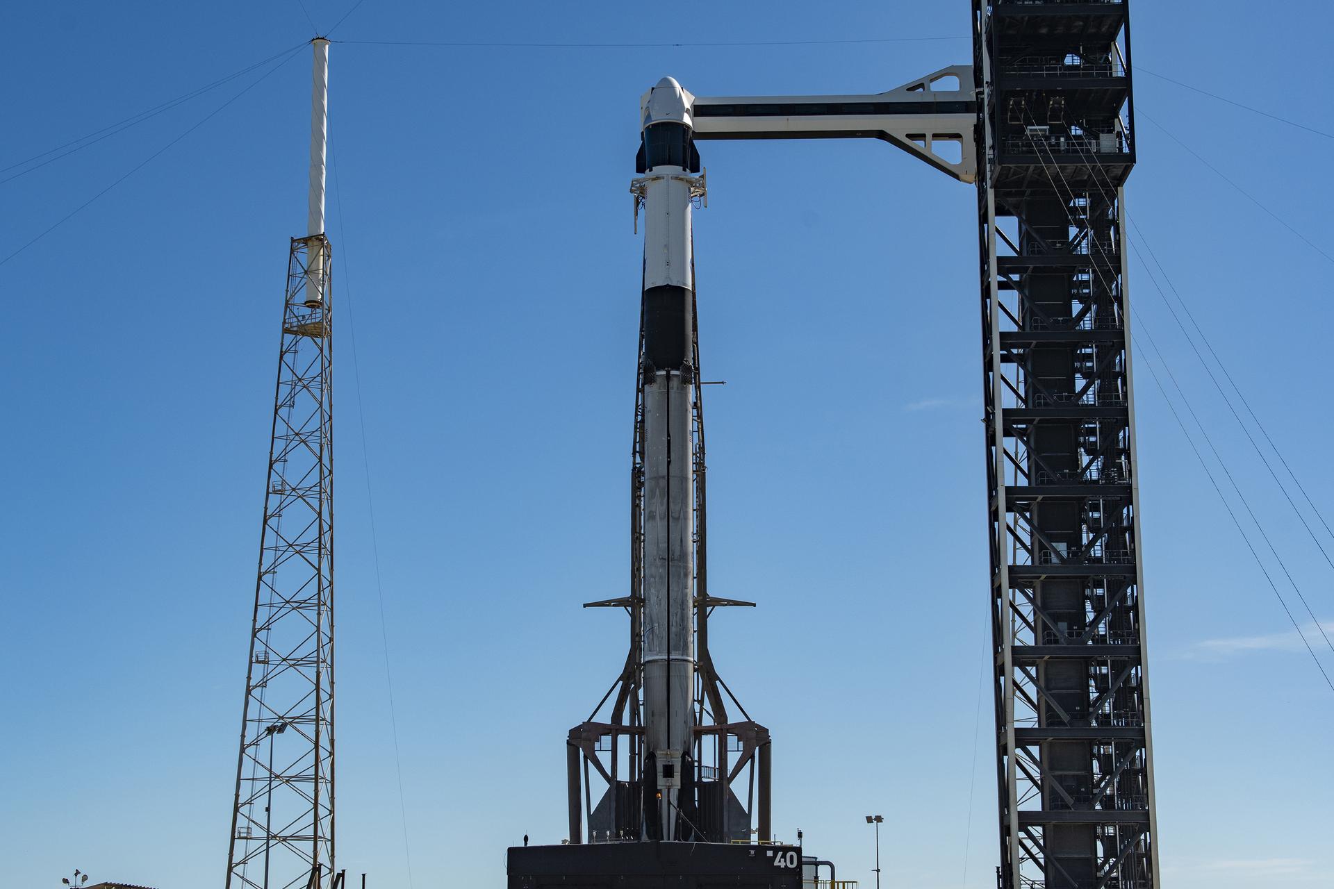 航天图片资料 · A SpaceX Falcon 9 rocket stands vertical on the launch pad at sunrise, with the crew access arm extended to the spacecraft and surrounding support towers silhouetted against a blue and orange sky.