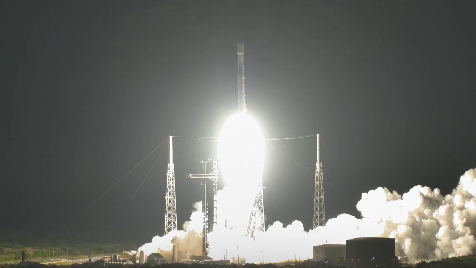 航天图片资料 · A rocket blasts into the black night sky over a launch pad, leaving a plume of white smoke in the wake of its white hot engine fire.