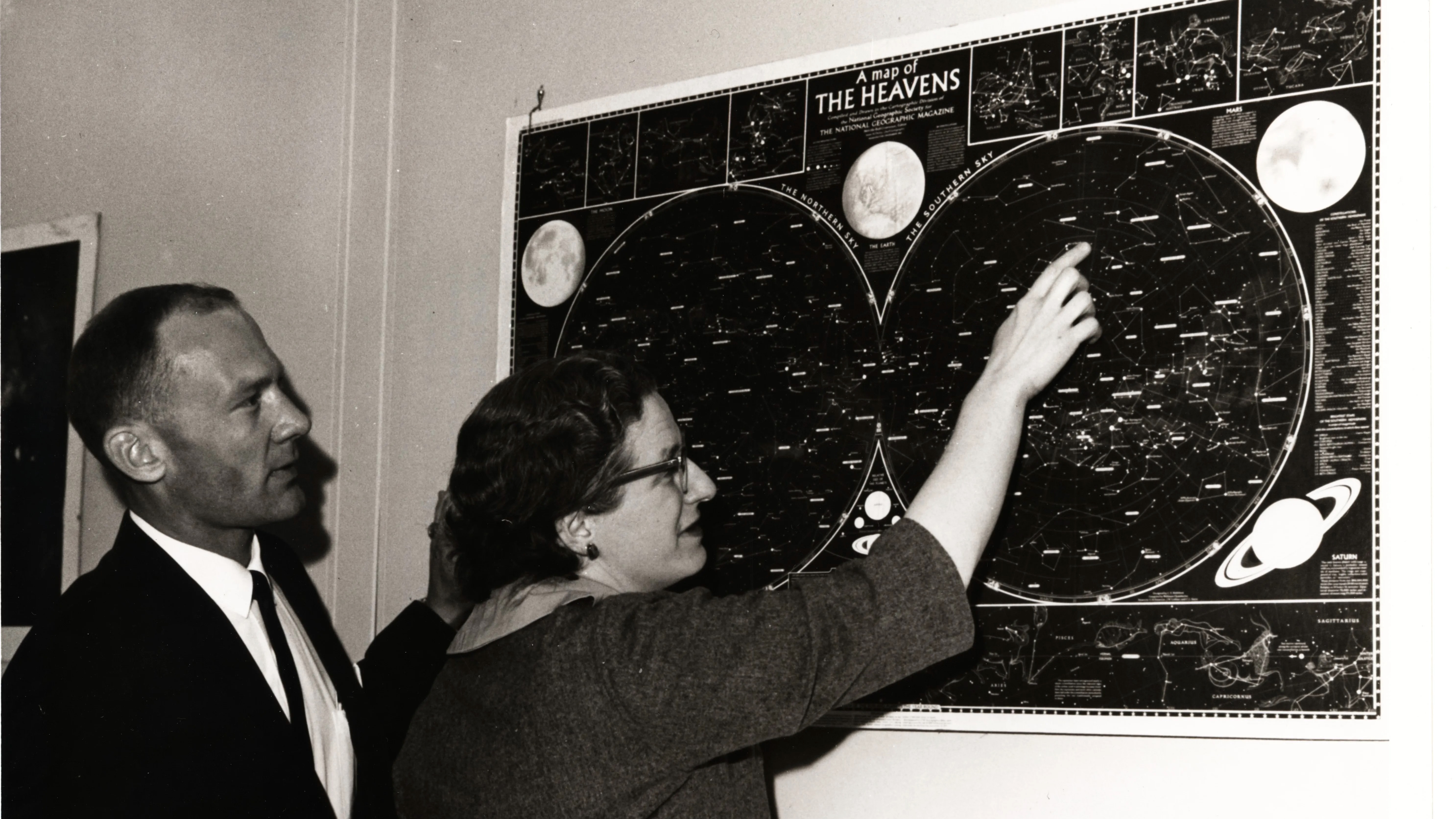 航天图片资料 · black and white photo of a woman showing a man a wall-mounted star chart