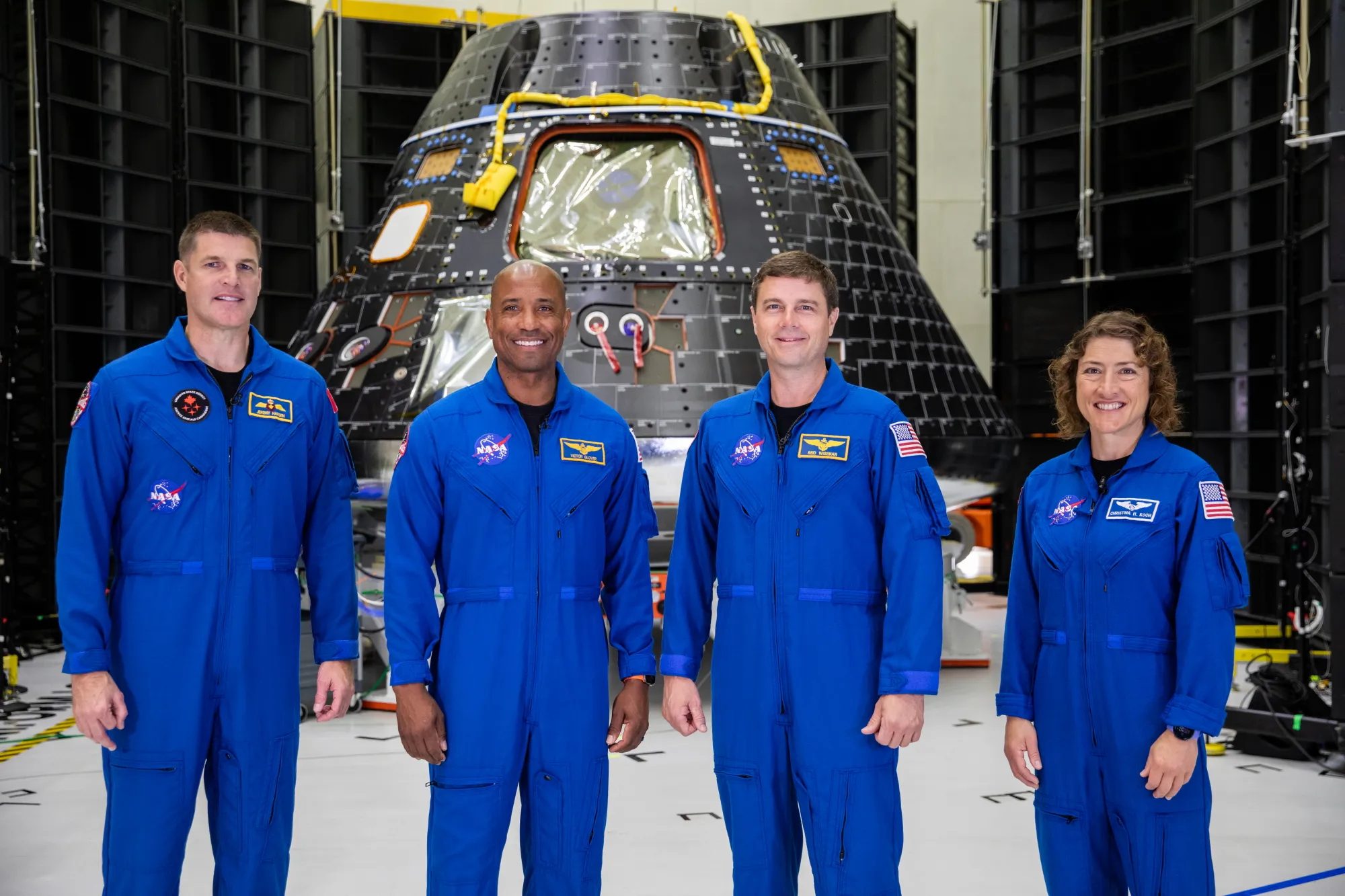 航天图片资料 · Four people in bright blue jumpsuits pose smiling in front of a spacecraft.