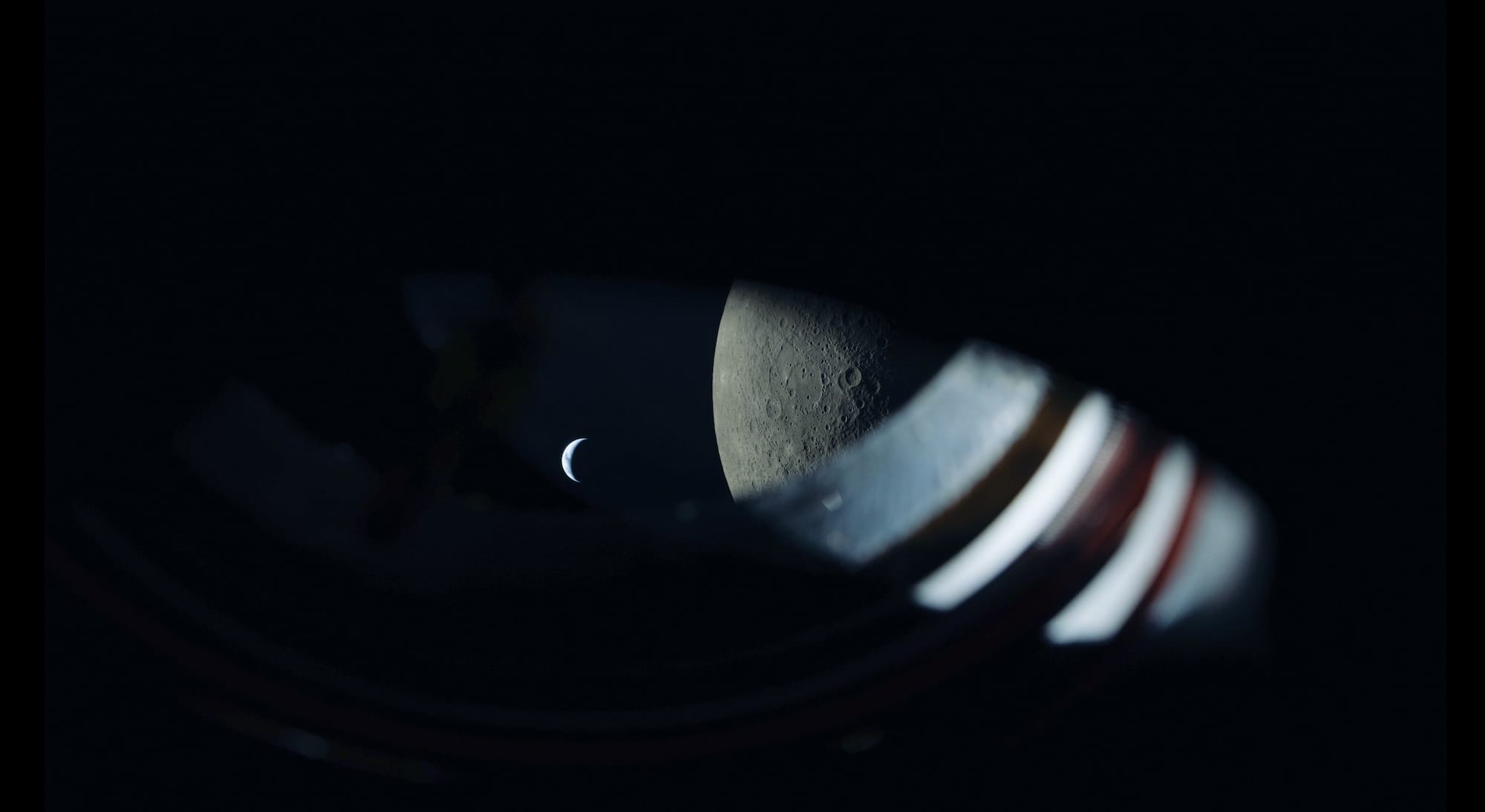 航天图片资料 · a view from the Artemis II spacecraft showing the edge of the window, the moon, and the earth as a tiny sliver