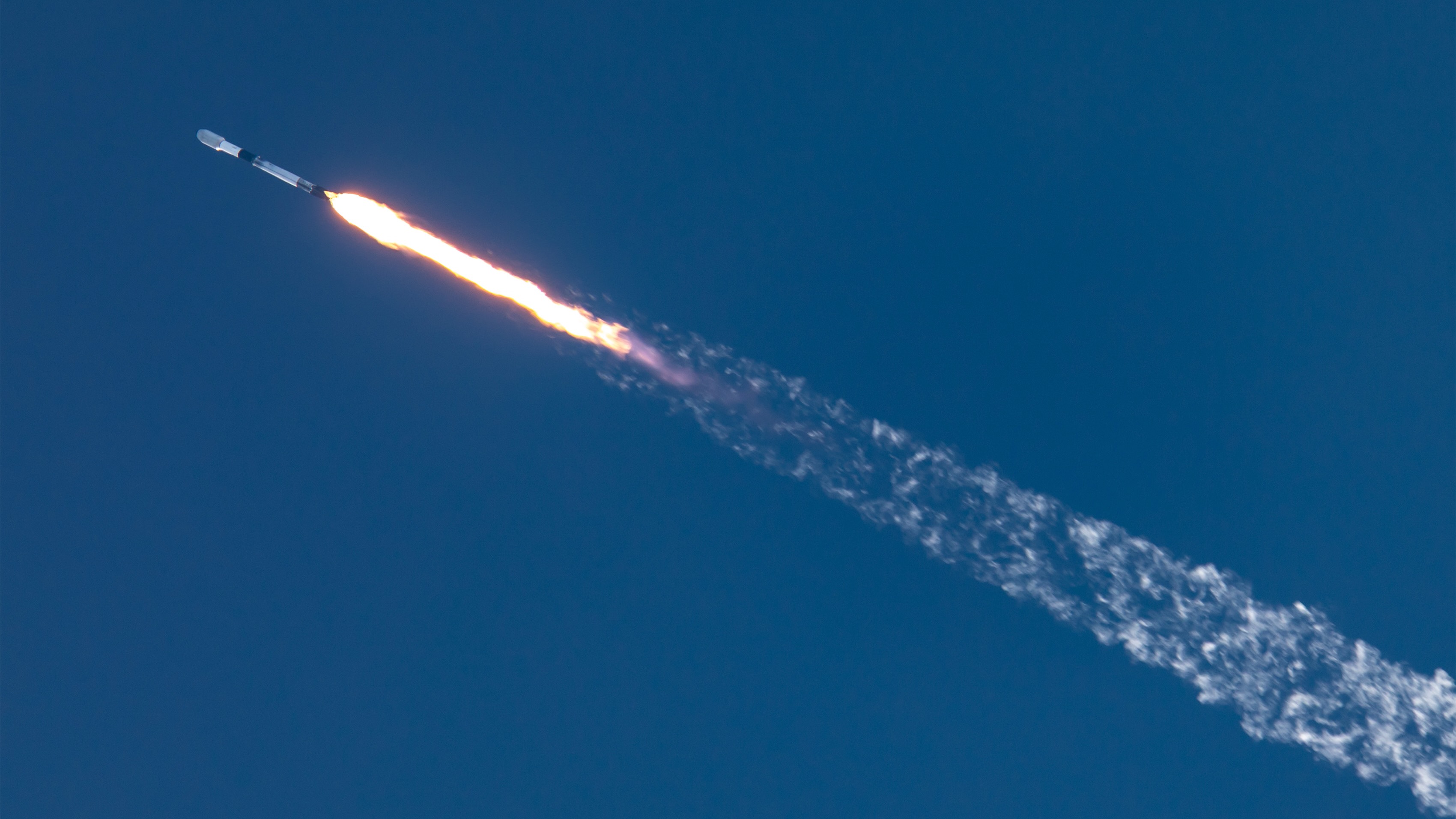航天图片资料 · long-distance photo of a black and white rocket rising diagonally through a blue sky