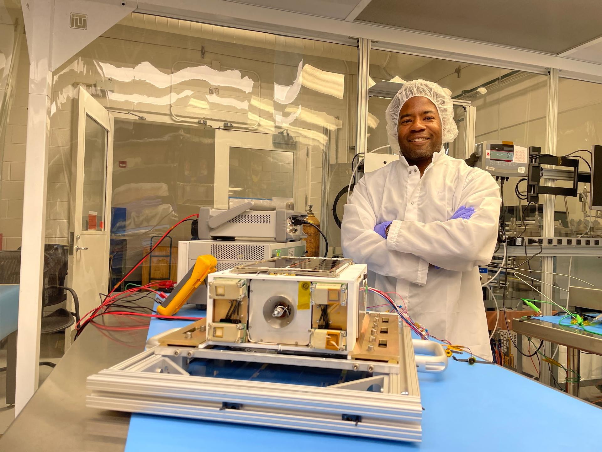 航天图片资料 · An Album of photos showing NASA engineers and technicians in white protective clean room suits working on a small, rectangular spacecraft module. They are shown inspecting the hardware on a laboratory workbench, wrapping it in silver foil, and loading it into a large, metallic vacuum chamber at NASA's Marshall Space Flight Center