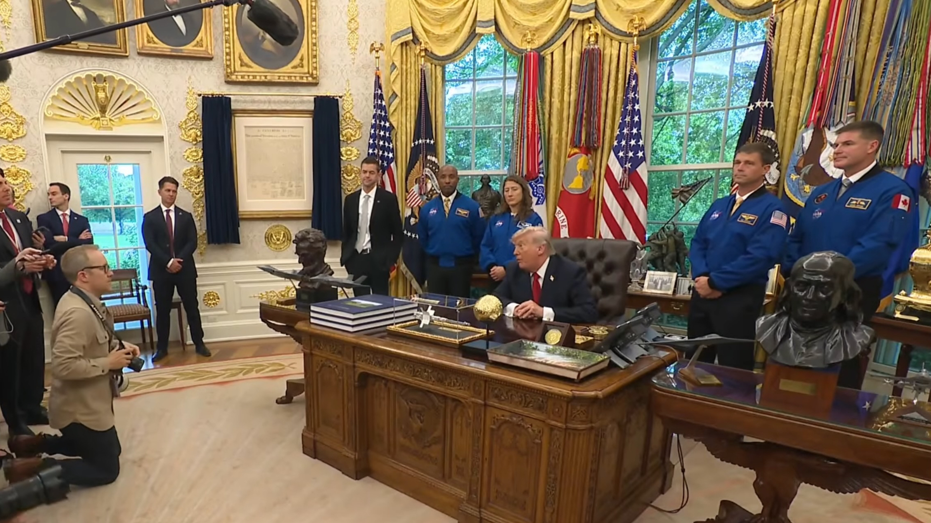 航天图片资料 · four people in blue flights stand behind a man in a suit sitting at a fancy desk
