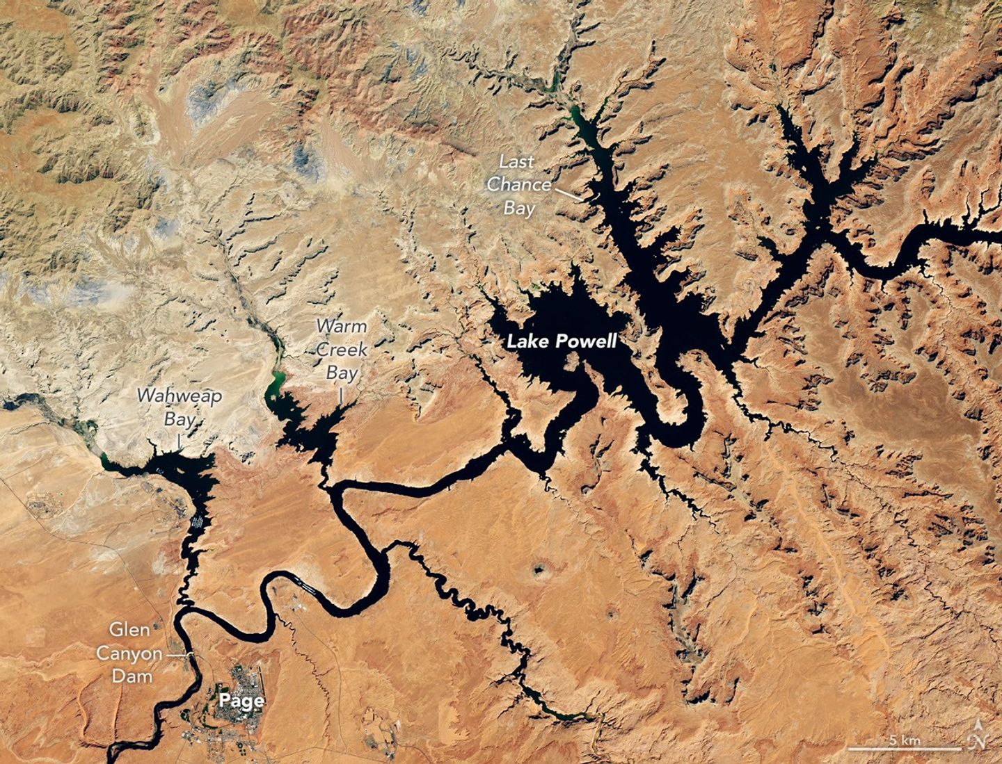 航天图片资料 · Water in Lake Powell is at record-low levels and looks like a wide river winding through a light orange desert landscape. The Glen Canyon Dam and the town of Page, Arizona, are visible in the lower left.