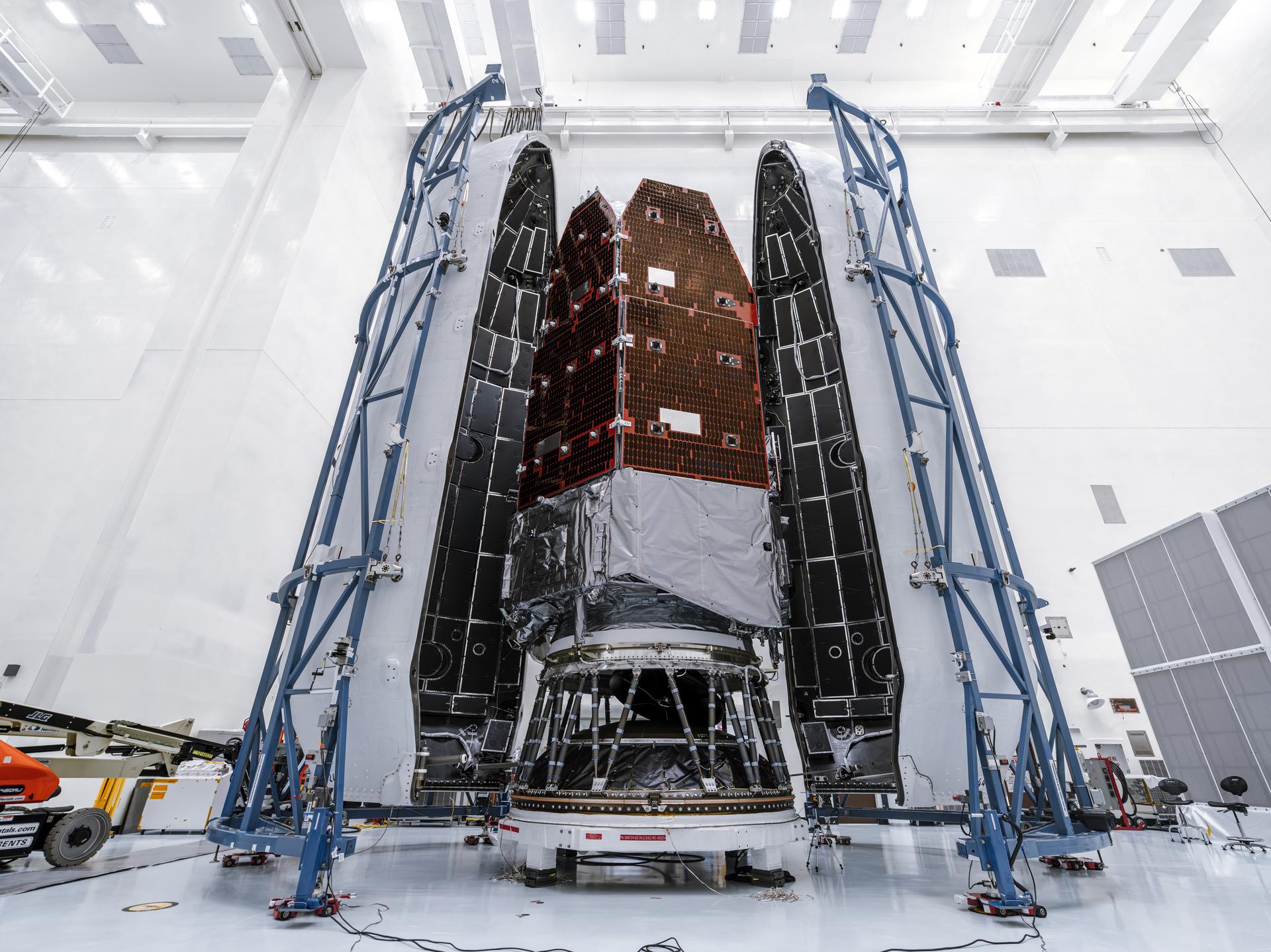 航天图片资料 · Full-height view of the Roman Space Telescope inside the tall payload fairing. Blue support structures stand on each side in the cleanroom environment.