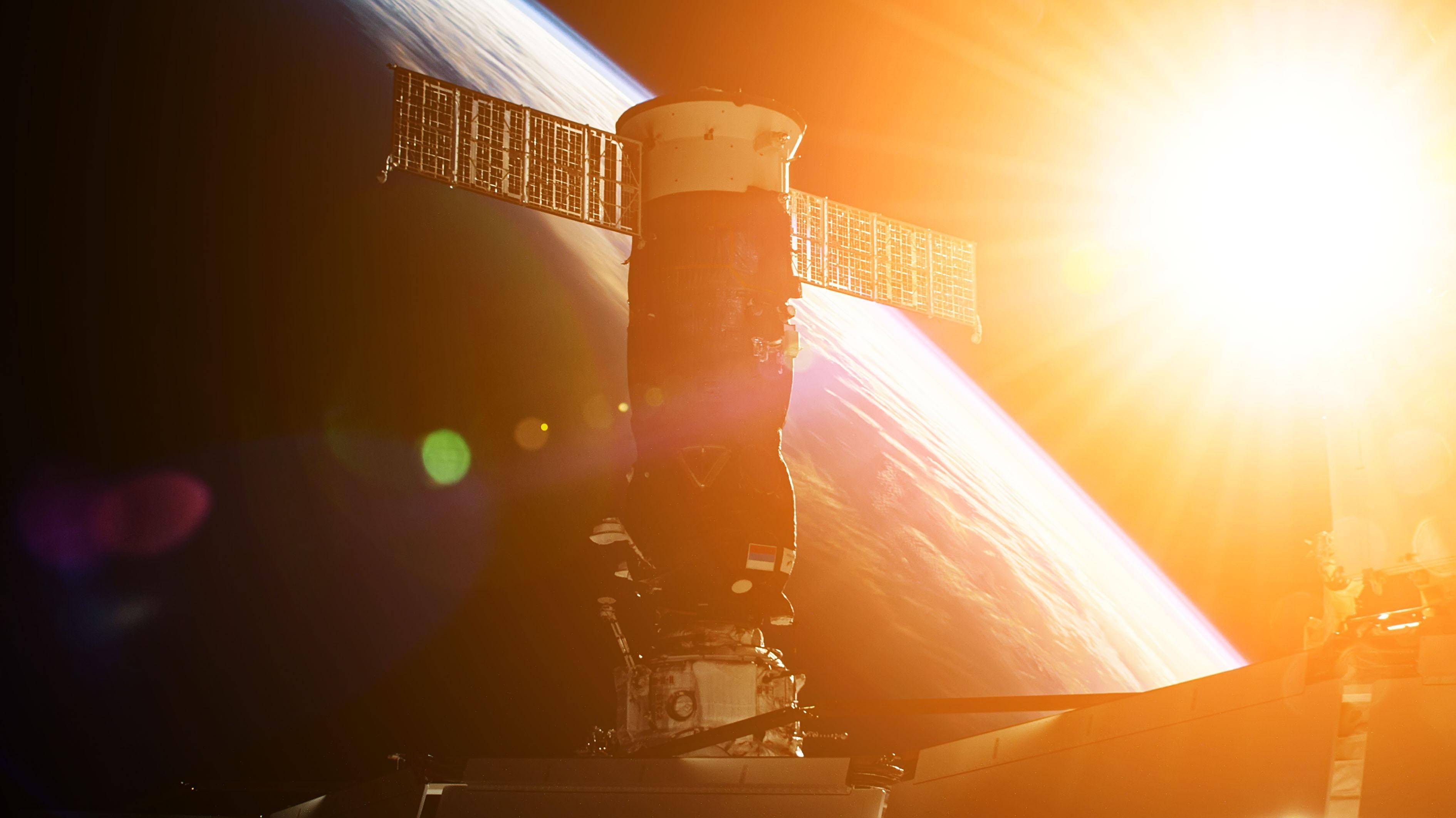 航天图片资料 · A spacecraft with solar panels orbiting above Earth with the sun behind it.