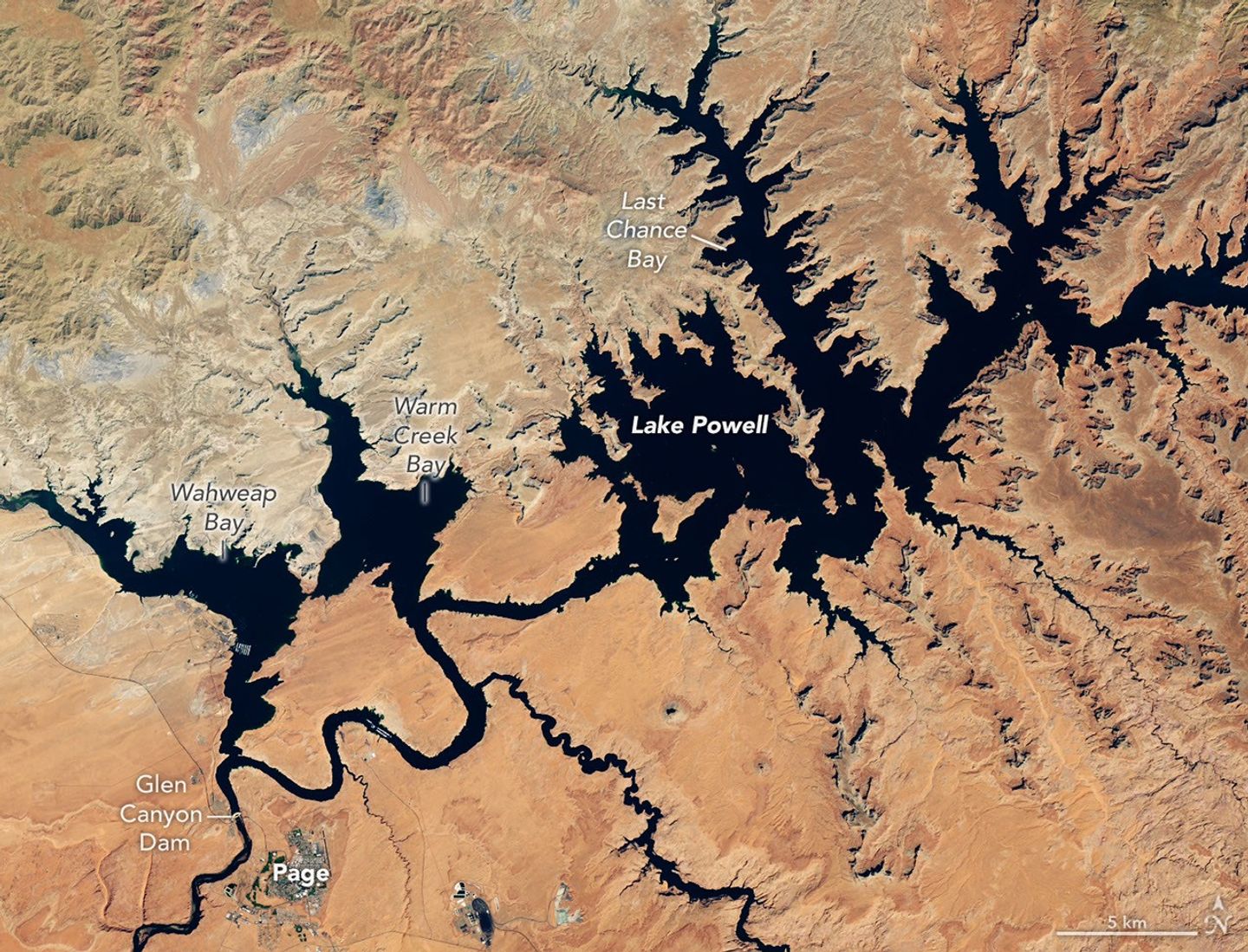 航天图片资料 · Dark blue water in Lake Powell fills several bays and branching canyons amid a light orange desert landscape. The Glen Canyon Dam and the town of Page, Arizona, are visible in the lower left.