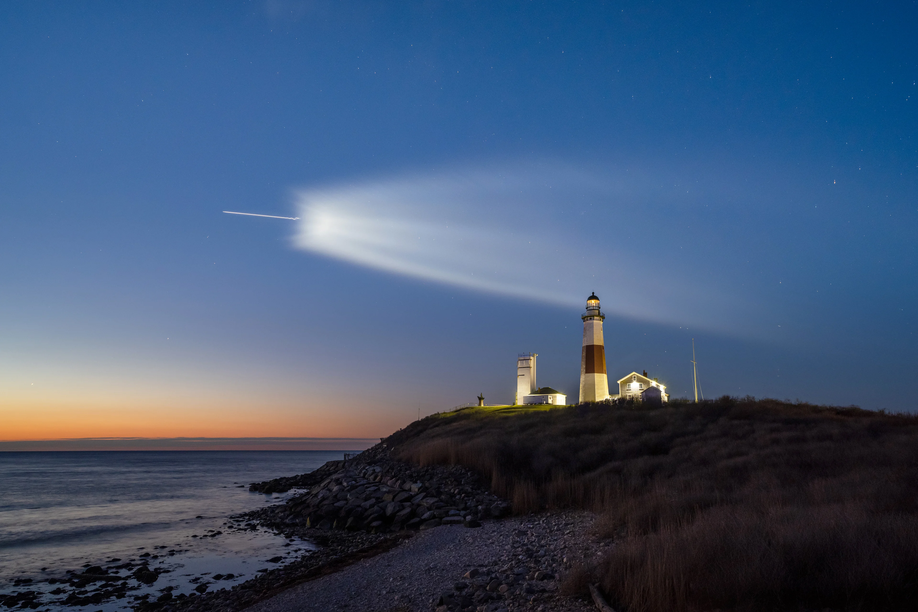 航天图片资料 · A rocket in launch over the ocean with a lighthouse in the foreground.