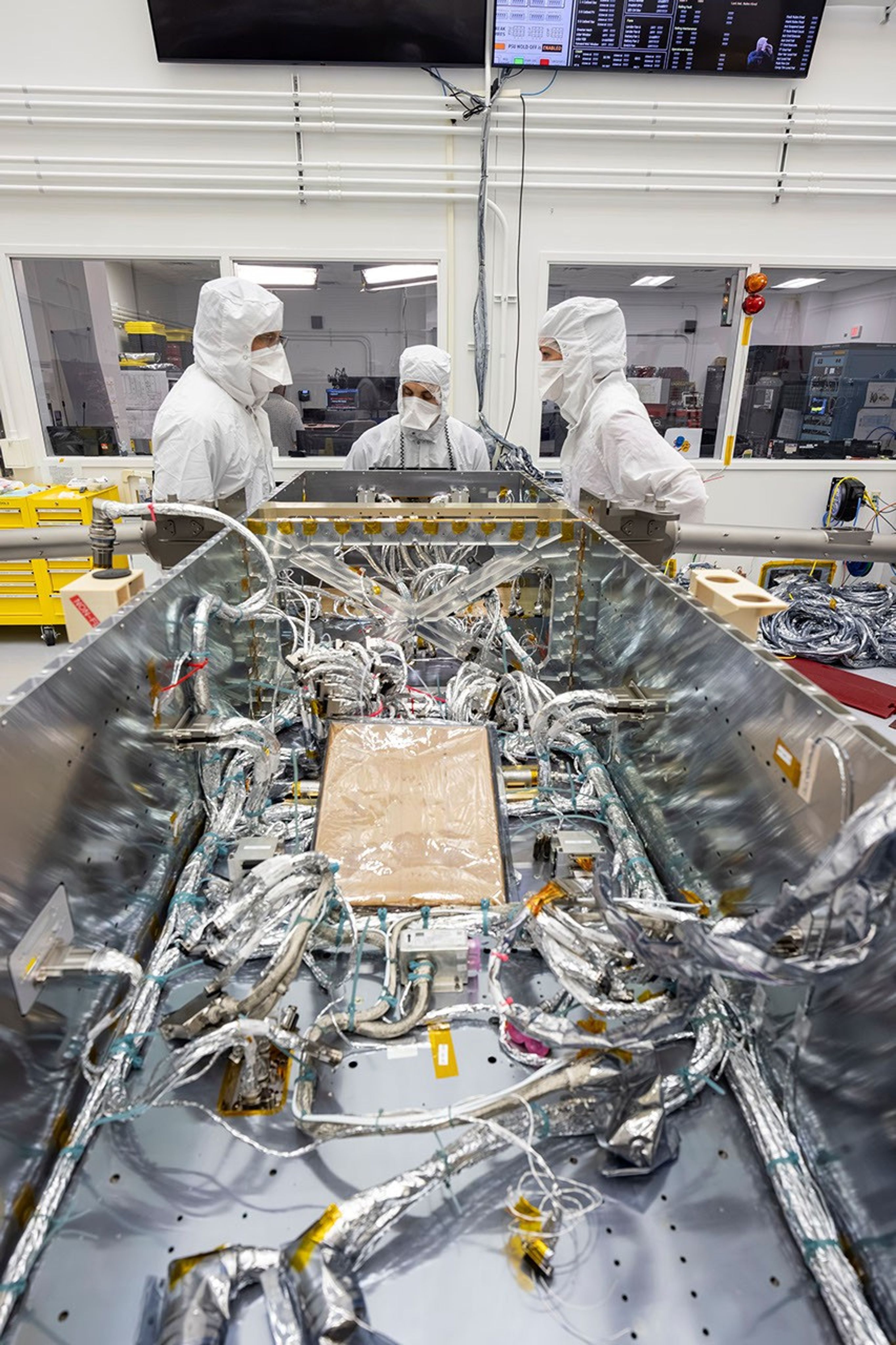 航天图片资料 · Technicians inside a clean room prepare to install electrical wiring to components inside of a spacecraft.