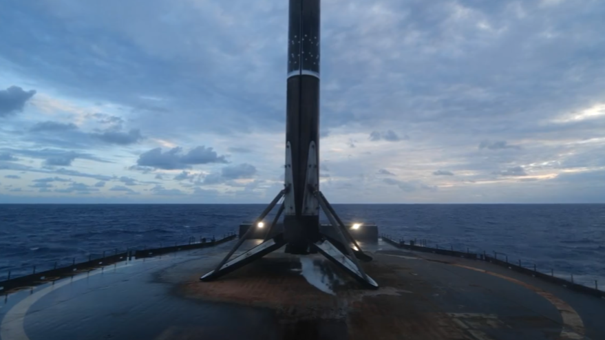 航天图片资料 · A sooty booster stands on 4 legs on a barge at sea.