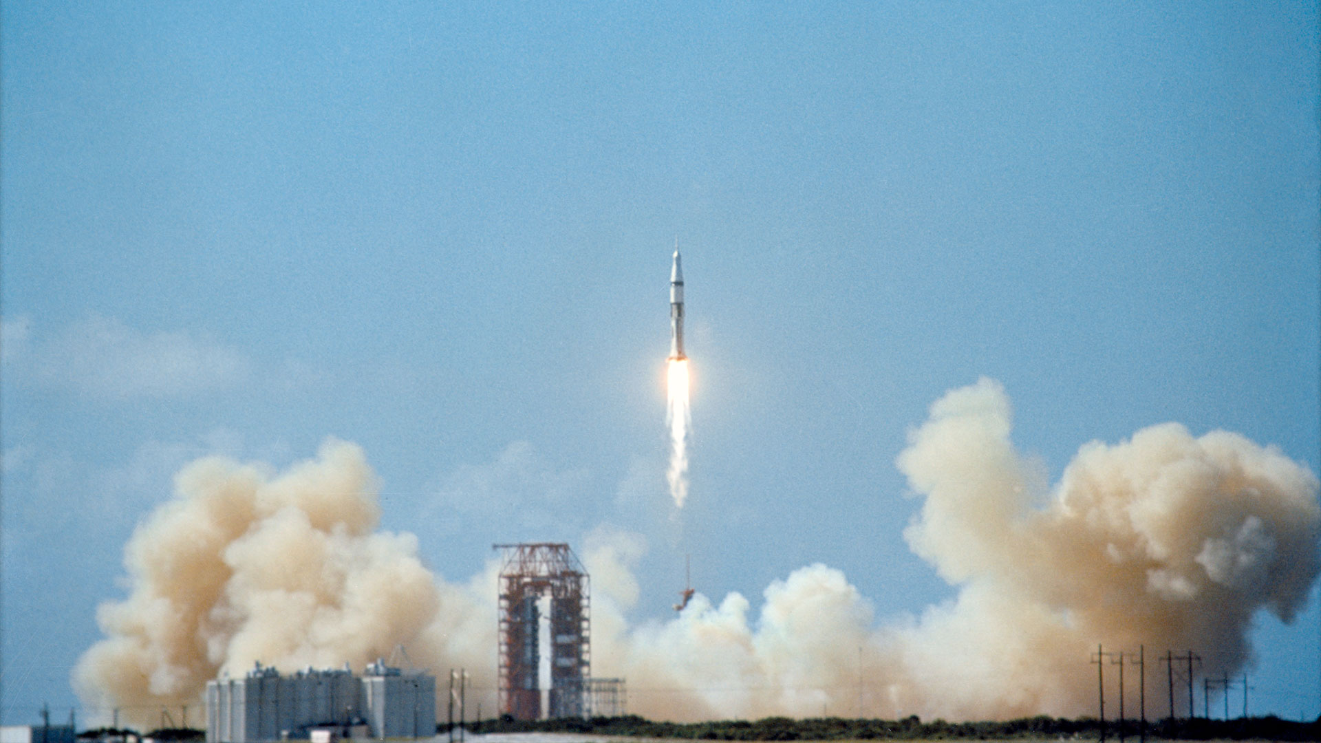 航天图片资料 · a white and black rocket lifts off into a blue sky leaving behind a plume spread across its launch site