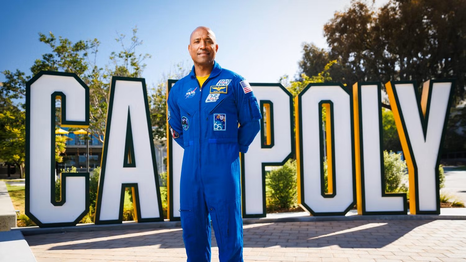航天图片资料 · A man in a blue jumpsuit stands in front of giant letters that read "CAL POLY"