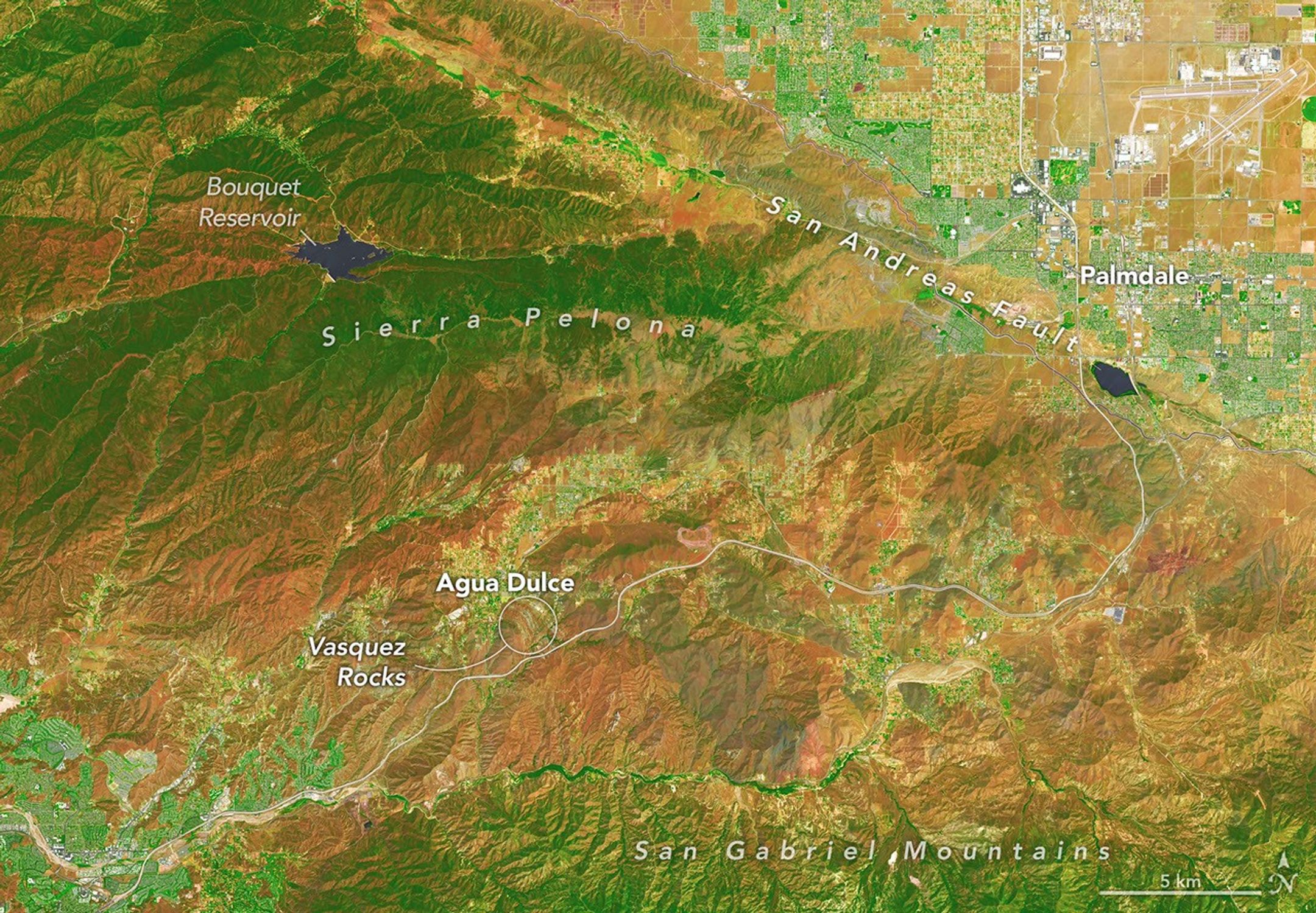 航天图片资料 · In this false-color image, areas with more extensive vegetation on the Sierra Pelona retain more moisture than the hills surrounding Agua Dulce, making the Sierra Pelona appear dark green in comparison to the rusty brown coloration of the lower hills. Vasquez Rocks appears as a patch of curved gray stripes near the center of the image.