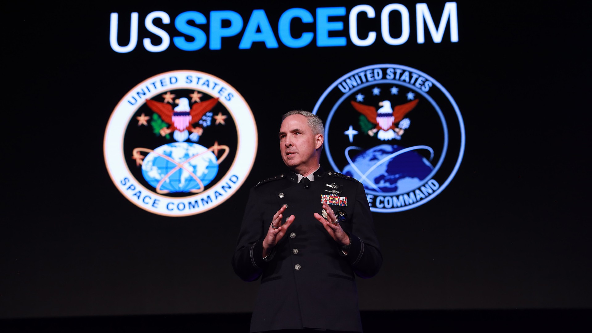 航天图片资料 · a man in a black military dress uniform speaks on a stage in front of an image of earth seen from space