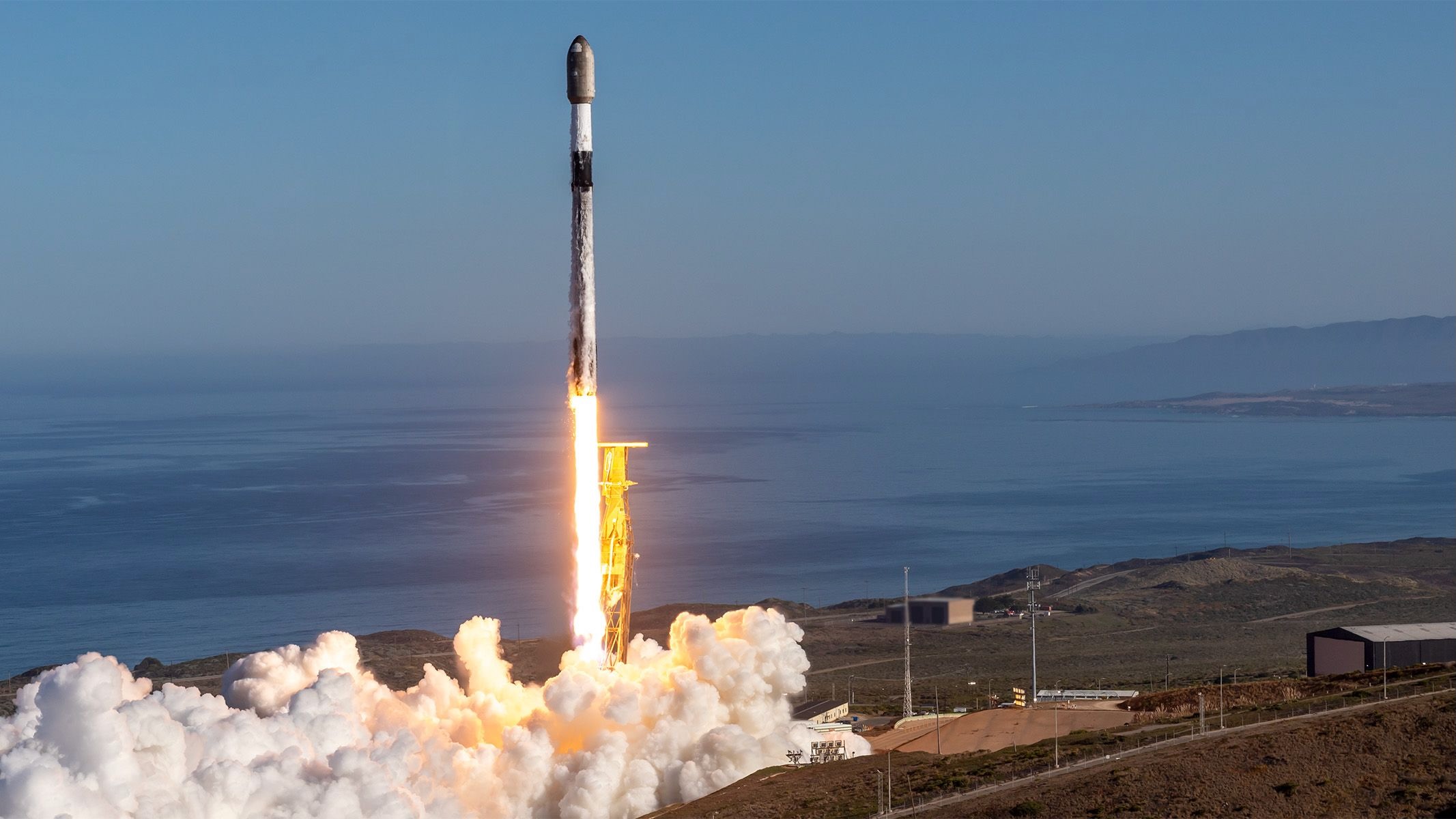 航天图片资料 · a black and white rocket launches into a blue sky from a seaside pad