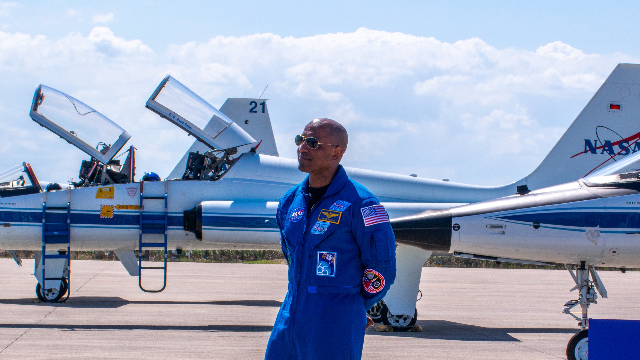 航天图片资料 · A man in a blue jumpsuit stands in front of giant a trio of NASA jets.