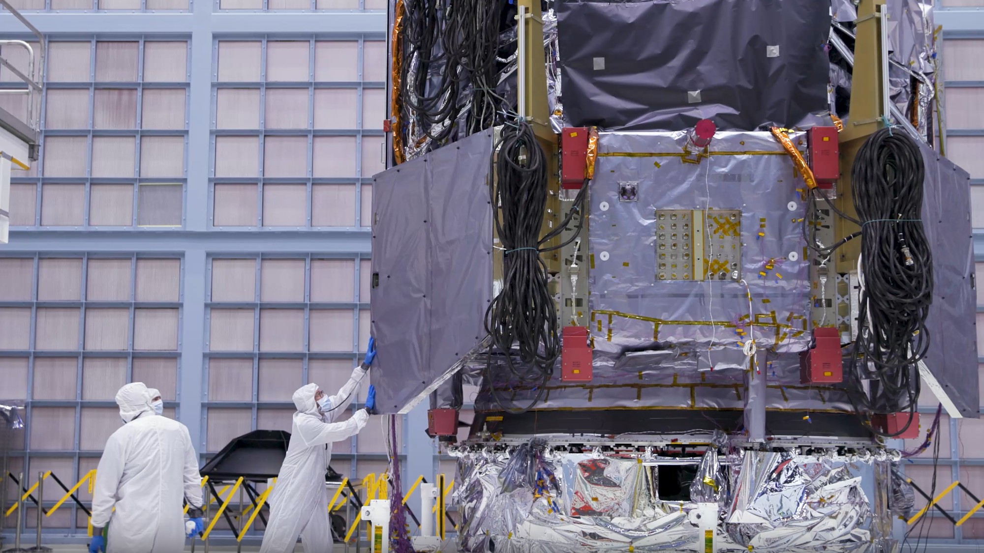航天图片资料 · technicians in clean suits in a hangar next to a large rectangular spacecraft wrapped in metallic foil