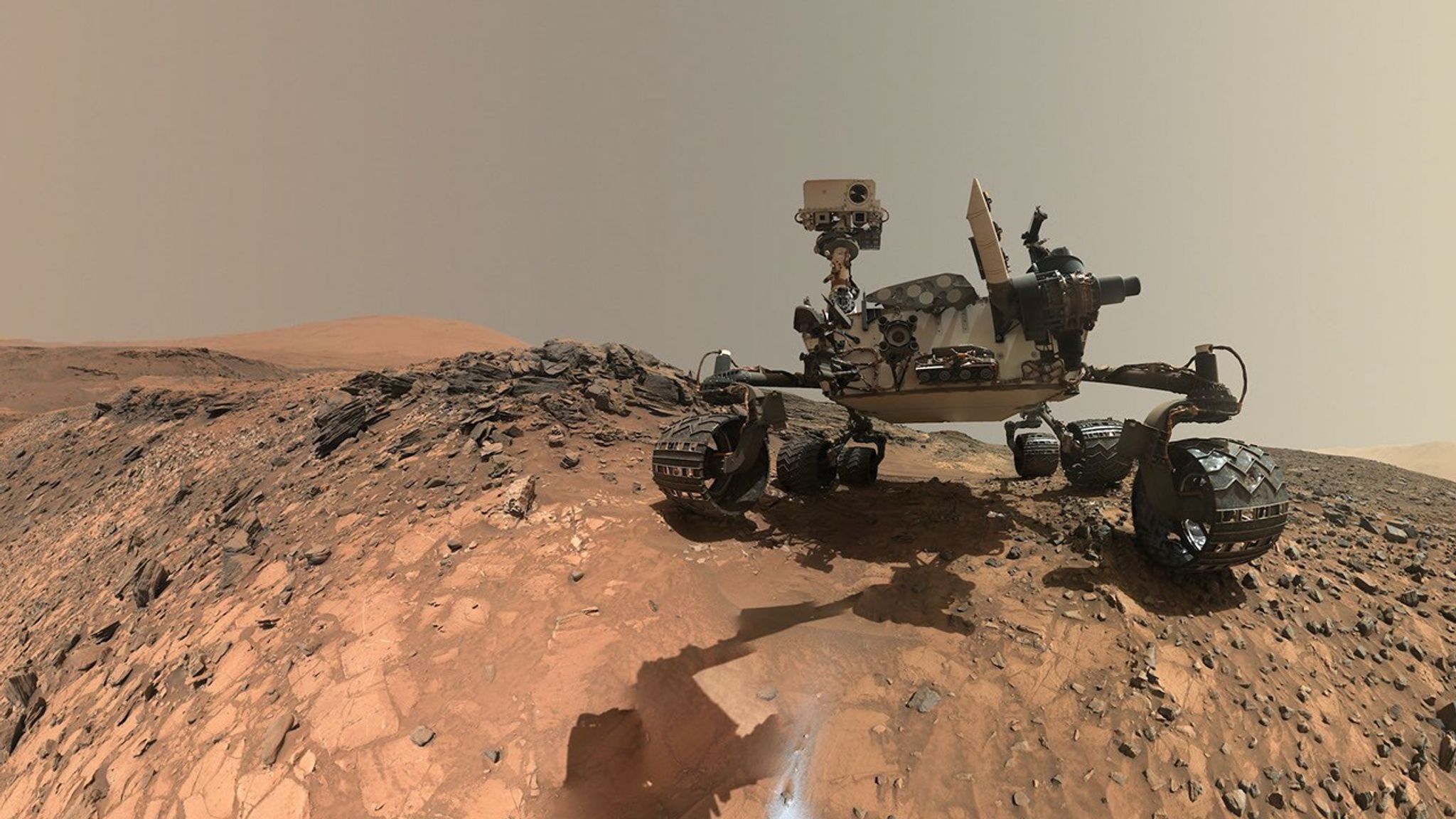 航天图片资料 · A rover sits on the hilly, orange Martian surface beneath a flat grey sky, surrounded by chunks of rock.