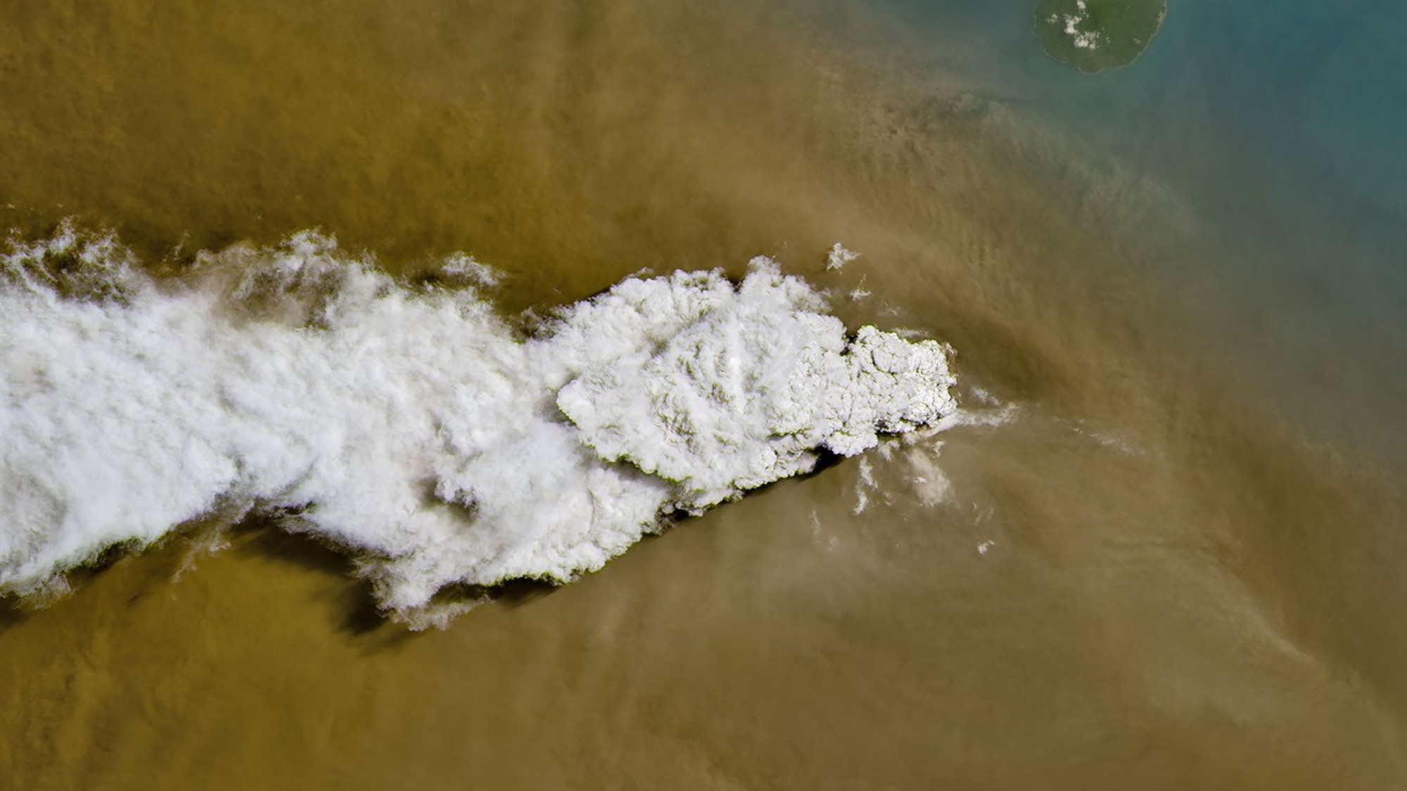 航天图片资料 · a plume of white-grey smoke rises from a small island, as seen from high overhead