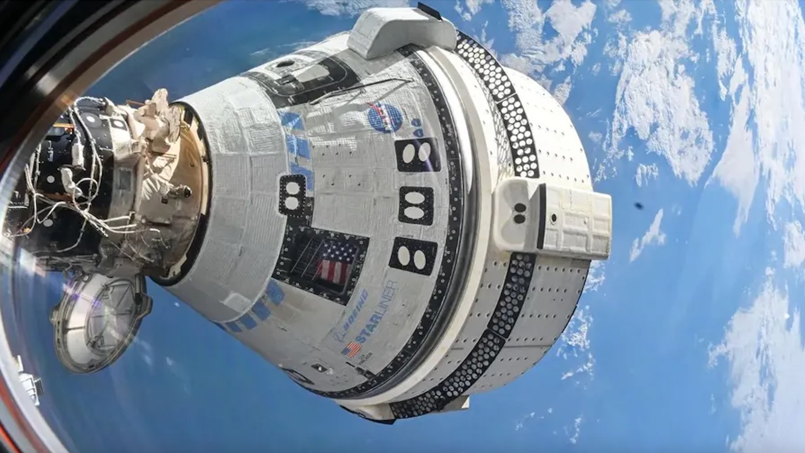 航天图片资料 · closeup view of a white conical spacecraft docked to the international space station, seen through the space station's window with clouds over the ocean in the background
