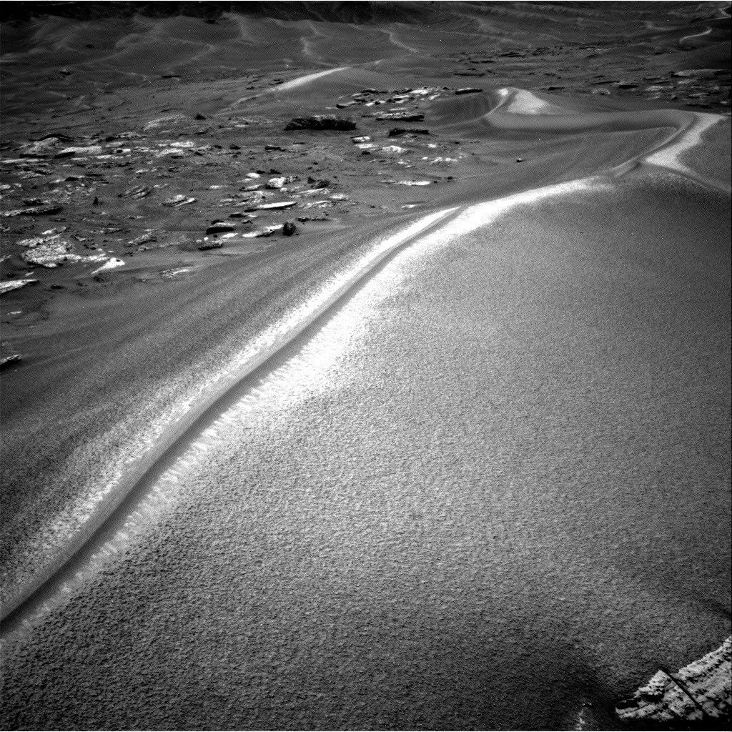 航天图片资料 · A black-and-white photograph from the Mars Curiosity rover showing a large, sweeping sand dune with a sharp, brightly sunlit crest. To the left are scattered flat rocks, and more rolling dunes stretch into the distant background.