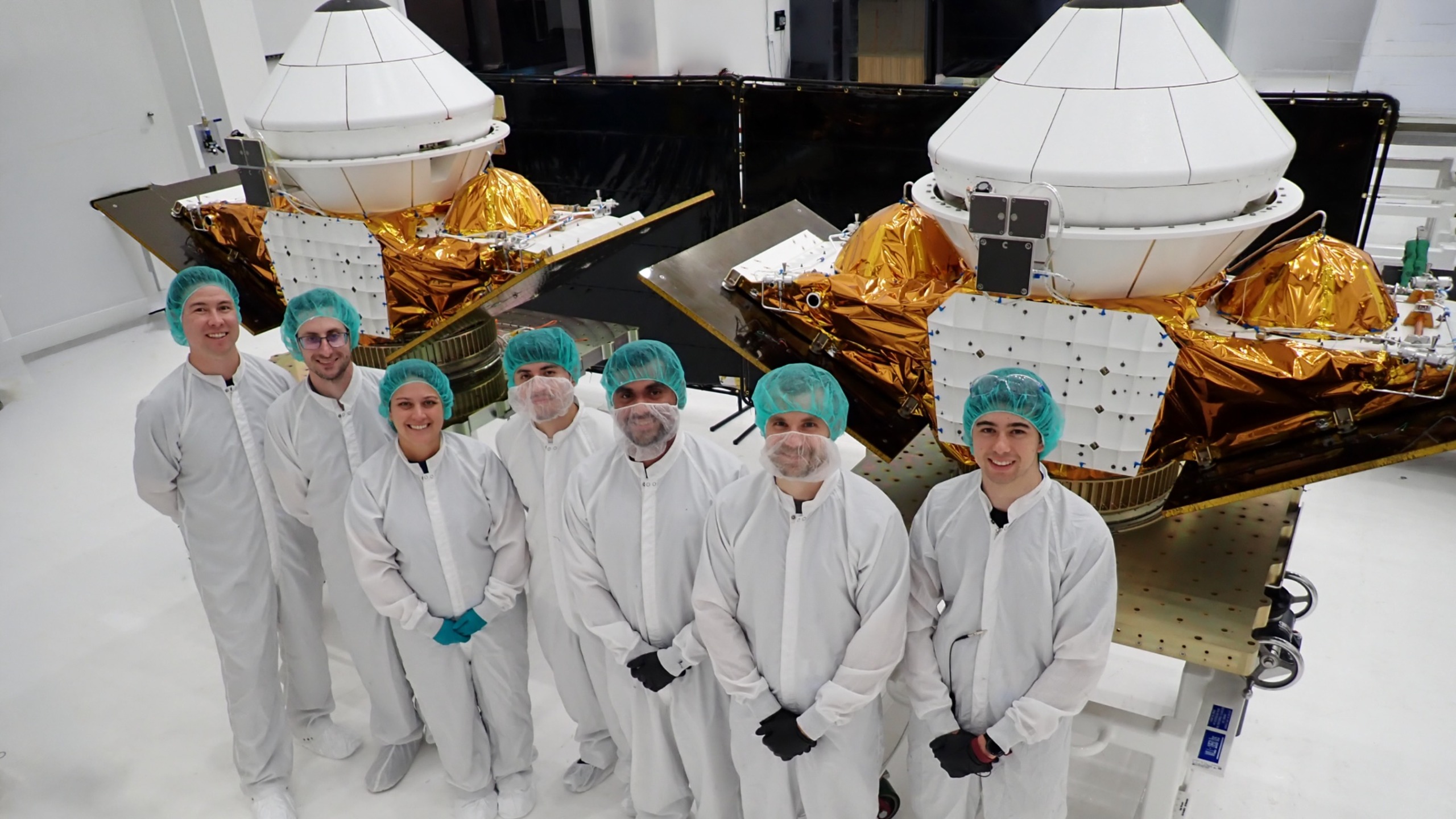航天图片资料 · seven people in white lab coats stand in front of two white cone-shaped spacecraft inside a white-walled cleanroom